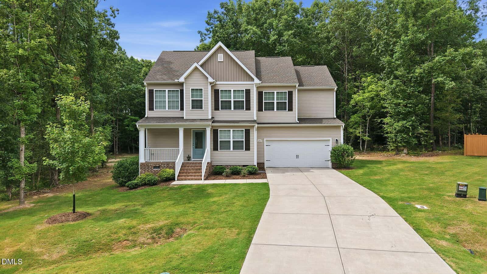 Two-story suburban house at 20 Shearin Lane, Youngsville, featuring a front porch, attached two-car garage, and a curved driveway, situated on a grassy lawn with surrounding trees under a clear blue sky.