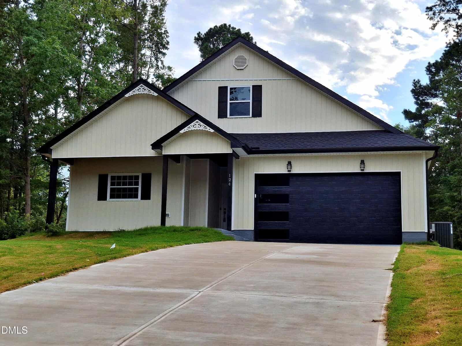Modern two-story house with white siding, black trim, and a black garage door, located at 124 Oklahoma Drive in Louisburg. The home features a gabled roof, a small covered porch, and a wide driveway, all surrounded by trees and grass.