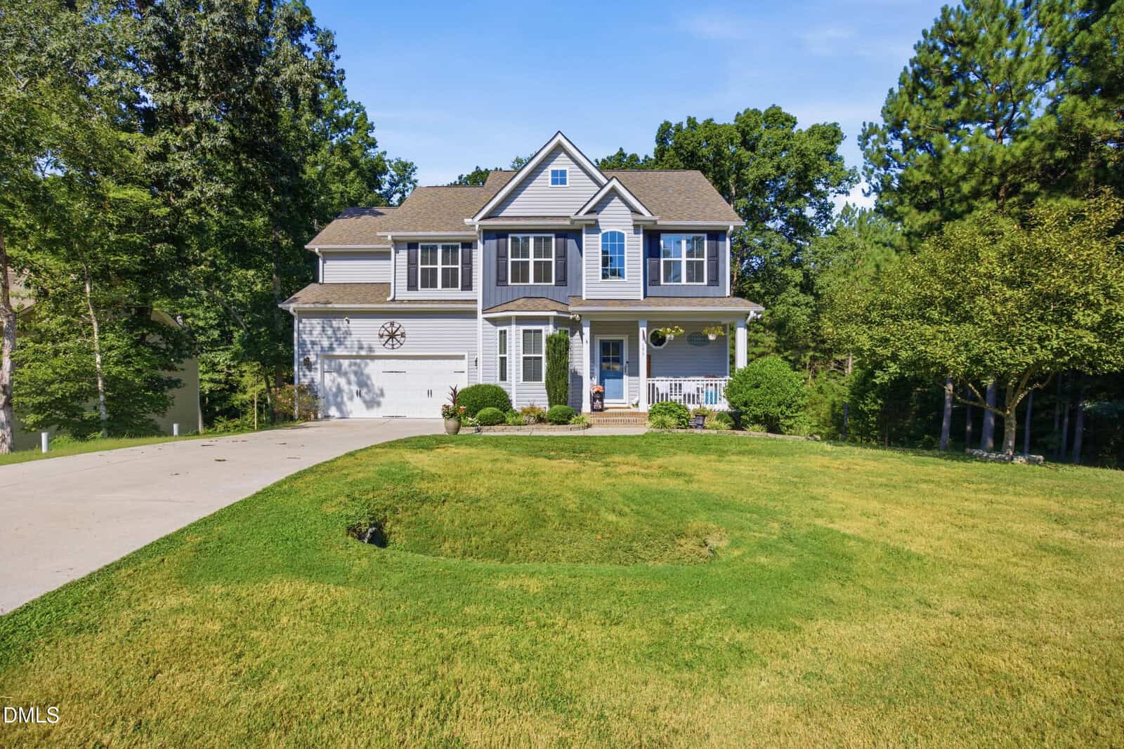 Two-story gray house with white trim, attached garage, front porch, and shutters. Located at 195 Timberwind Road in Franklinton, it sits on a large, green lawn with trees in the background and a curved driveway leading to the garage. Sunny day with a clear blue sky.