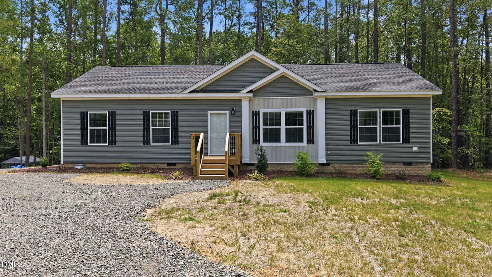 Single-story gray house with white trim, black shutters, a small front porch, and gravel driveway located at 211 Old North Carolina 75 in Stem, set against a backdrop of tall pine trees and green grass.