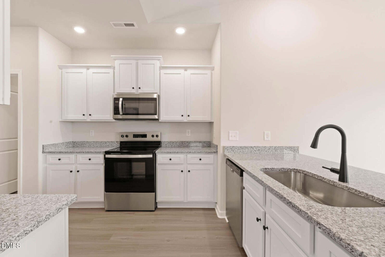 Modern kitchen with white cabinets, stainless steel appliances, black faucet, granite countertops, electric stove, microwave, dishwasher, and light wood flooring under bright recessed lighting.