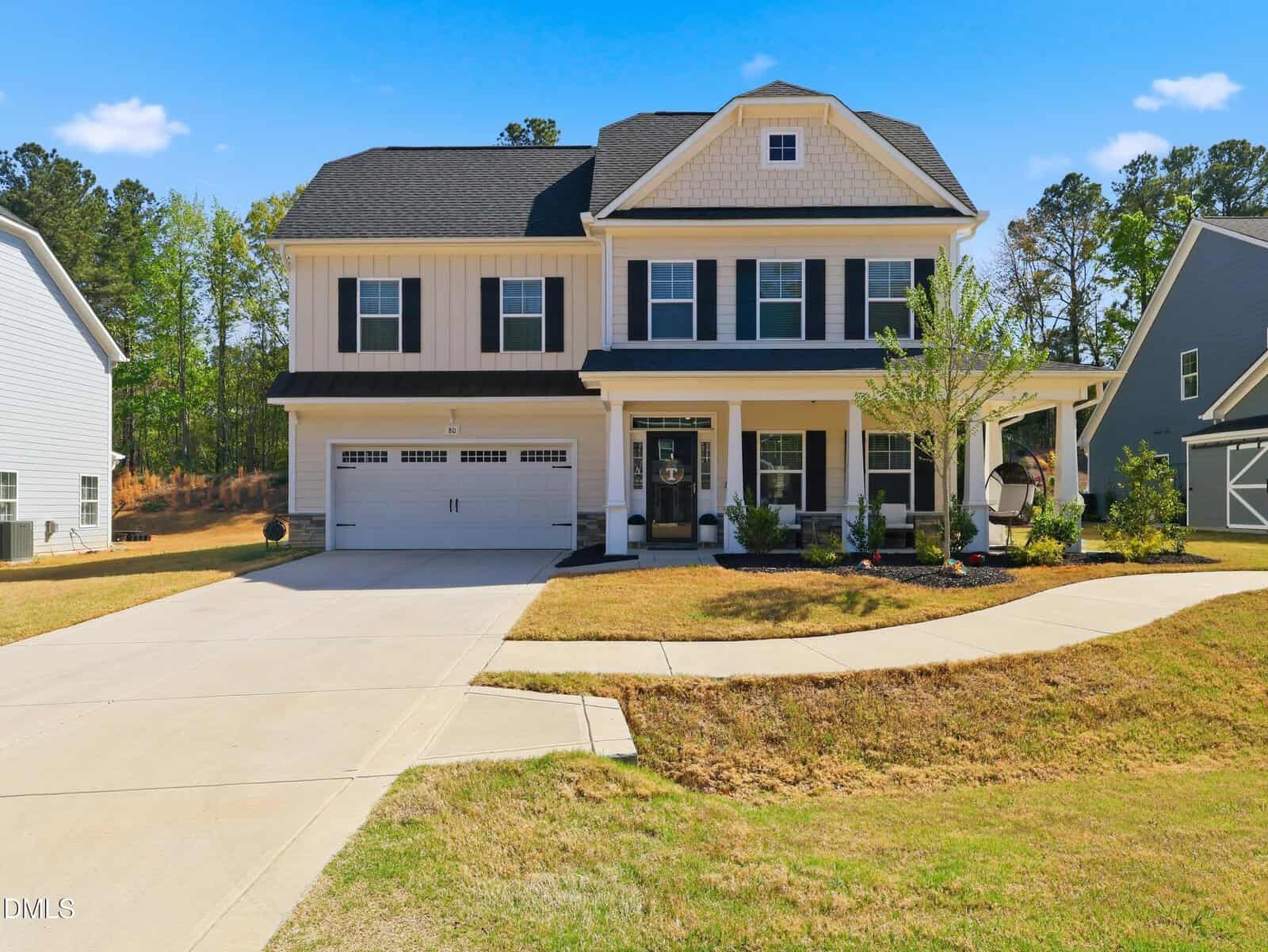 Two-story suburban house at 80 Vast View Way, Youngsville, with black shutters, a double garage, covered front porch, and a landscaped yard, on a sunny day with clear blue sky and trees in the background.