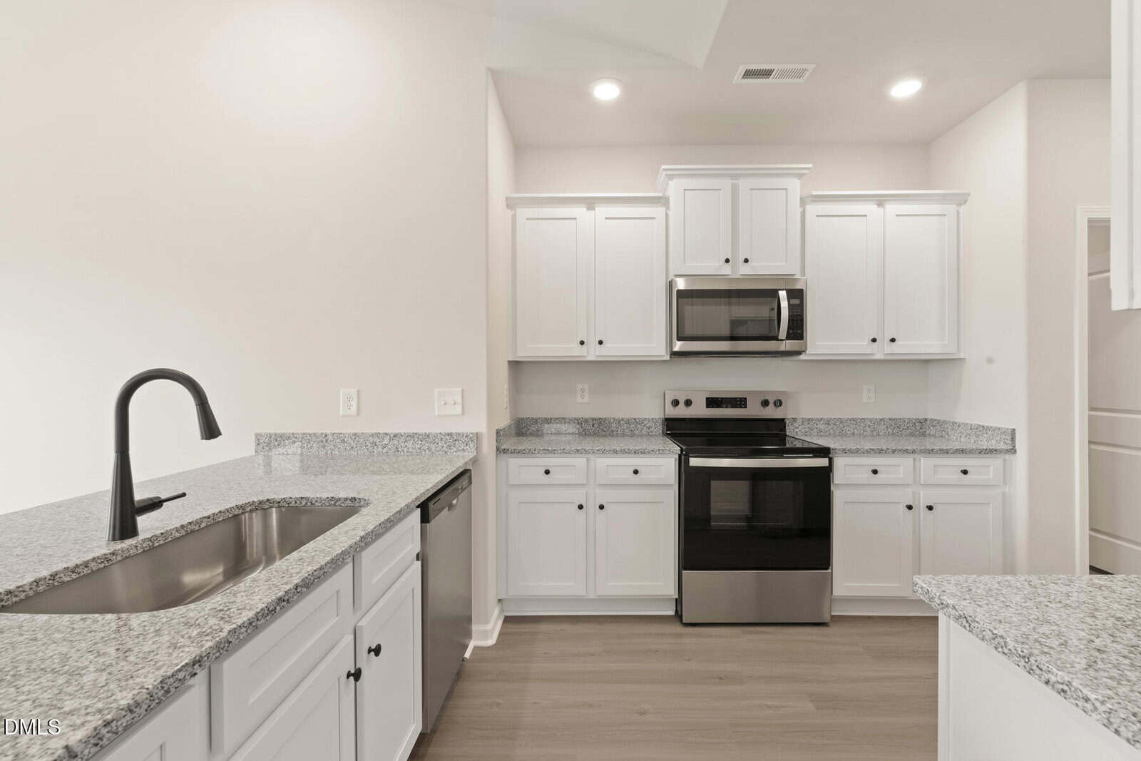 Modern kitchen with white cabinets, granite countertops, stainless steel appliances, electric stove, built-in microwave, dishwasher, and a black faucet on the sink. Light wood flooring and neutral walls create a bright, clean space.