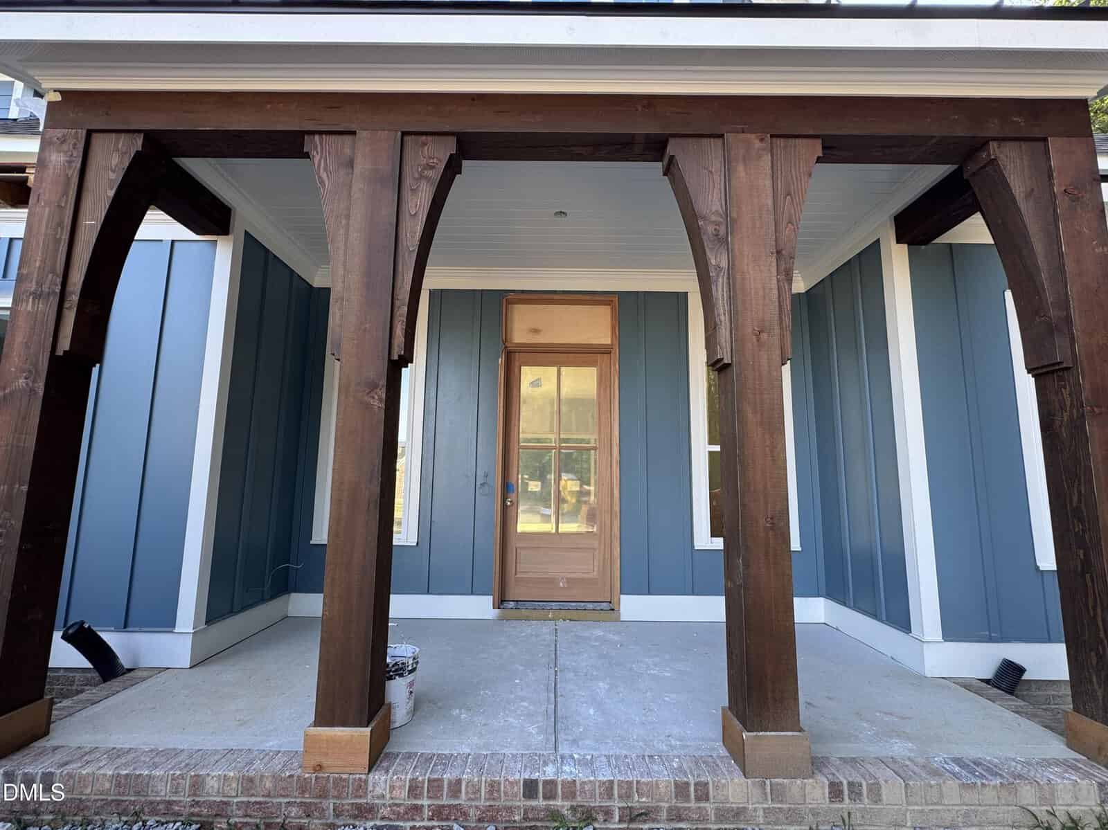 A front porch with dark wooden columns, blue siding, a wooden door with glass panels, and brick steps leading up to the entrance.