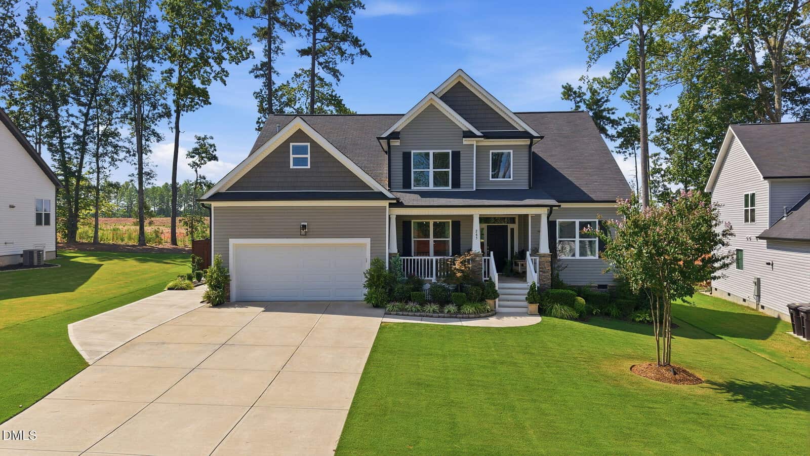 Two-story gray house with a white garage and front porch, surrounded by a well-manicured lawn, shrubs, and trees. Located at 245 Stephens Way in Youngsville, this home features a concrete driveway leading up to the house on a sunny day.