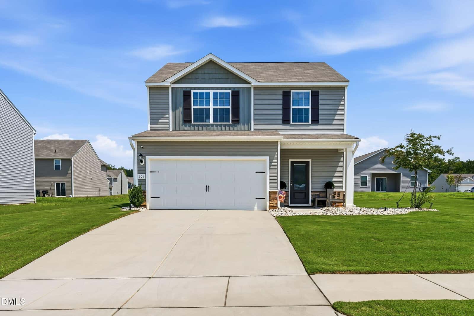 Two-story gray house with white trim, front porch, and attached two-car garage, situated on a neatly manicured lawn with a clear blue sky in the background.