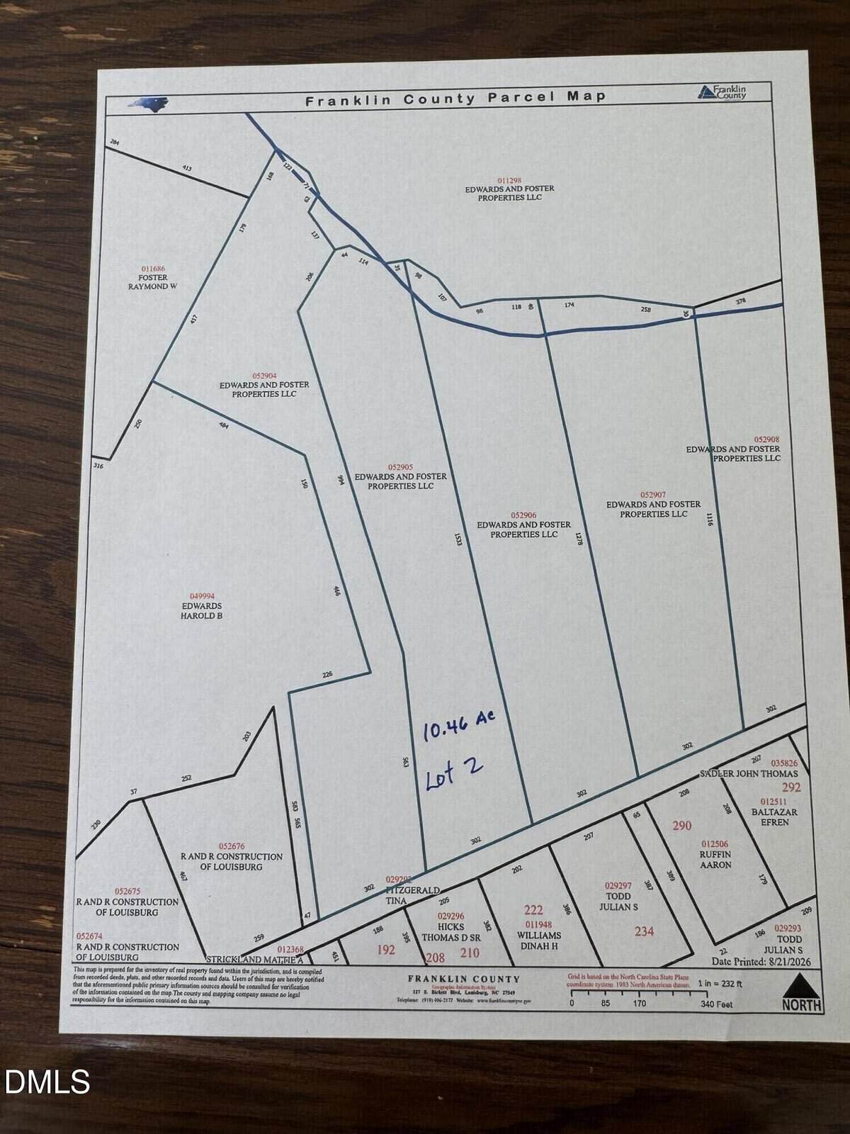 A printed Franklin County parcel map on a wooden table shows outlined property plots. Lot 2 Sutton Road, marked with “10.46 AC,” is hand-written in blue ink near the center of the image, highlighting its location near Louisburg.
