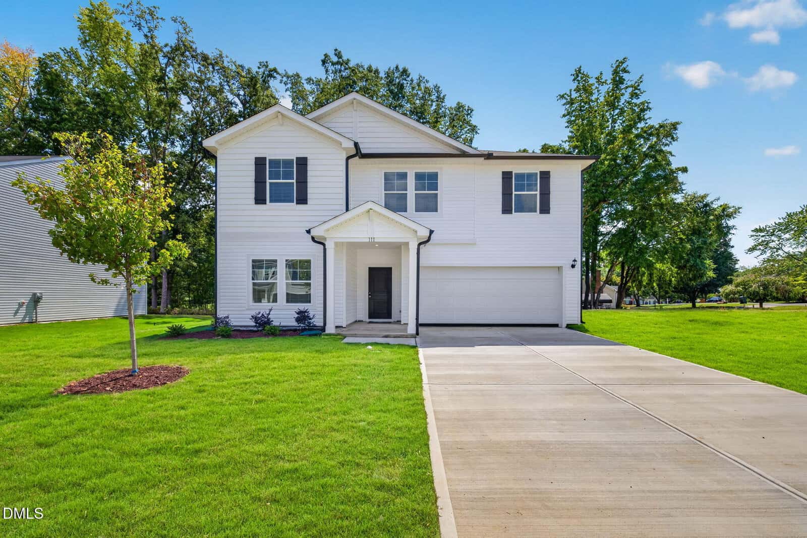 A modern two-story white house with black shutters, a covered front porch, and an attached two-car garage located at 111 Airdale Drive, Oxford. The home sits on a neatly manicured lawn with a young tree and a long concrete driveway.