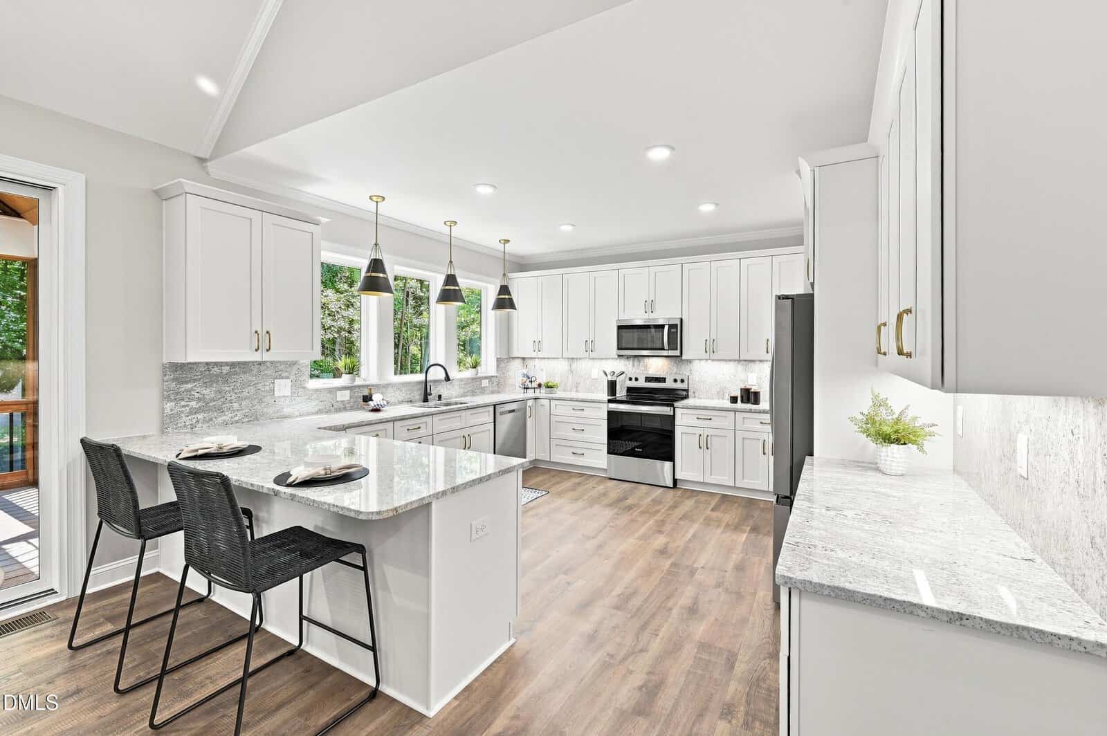 Modern white kitchen with marble countertops, stainless steel appliances, pendant lights, two black barstools at an island, large windows, wood flooring, and light gray backsplash.
