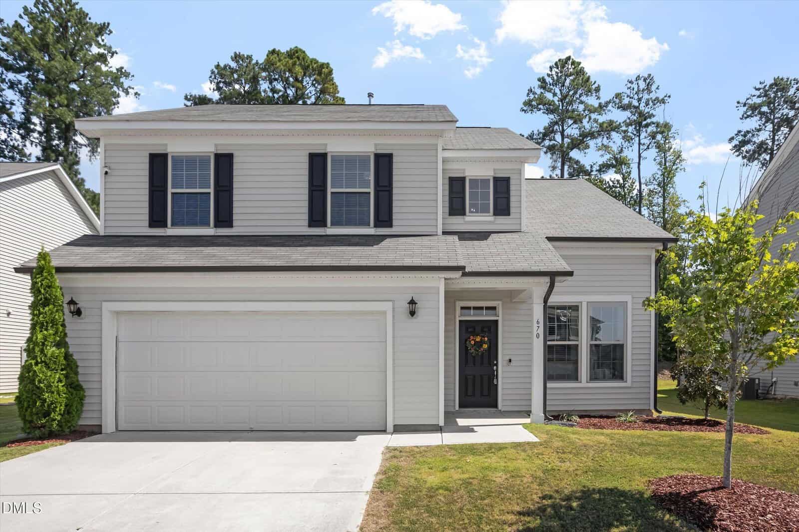 Two-story suburban house with white siding, black shutters, and a double garage at 670 Hawksbill Drive in Franklinton. A small tree and neatly trimmed lawn are in front, with tall trees in the background under a partly cloudy sky.