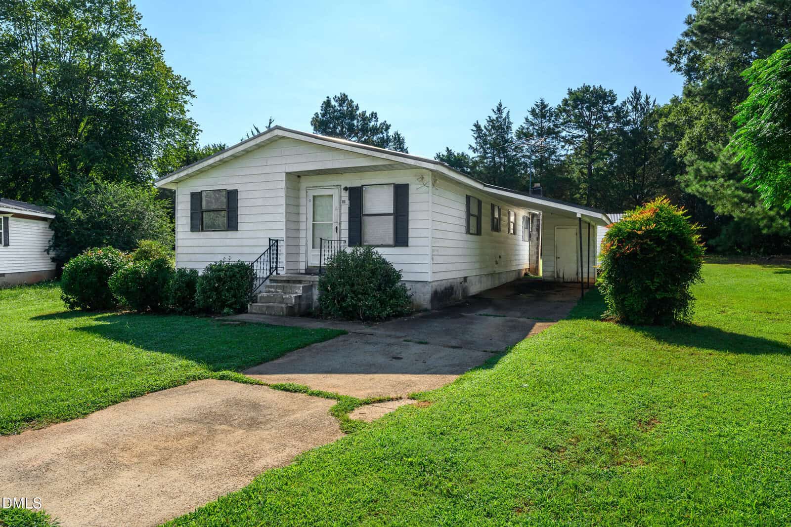 Charming single-story white house with black shutters, located at 111 Brown Circle in Norlina. Enjoy a small front porch with steps and neatly trimmed bushes along the front. A driveway leads to a convenient carport on the right, while a green lawn and mature trees surround the property for added privacy and curb appeal.