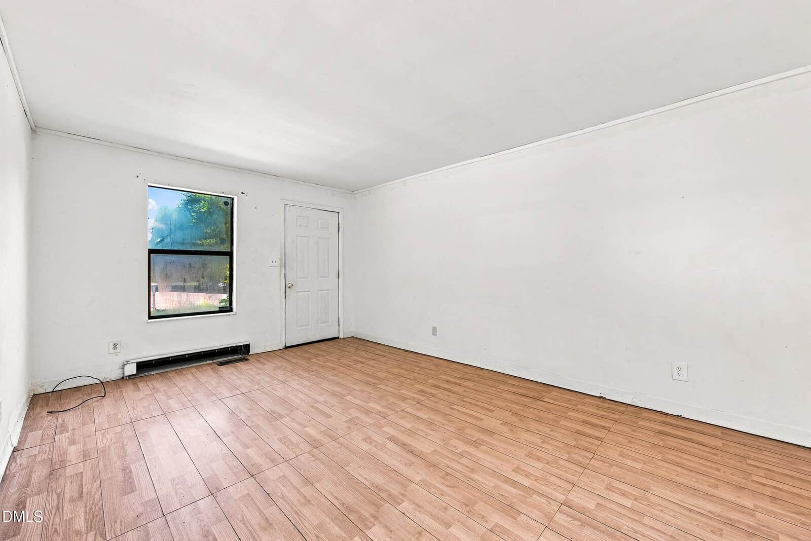 Empty room with white walls, wood-style flooring, a single window, and a closed white door. A black baseboard heater is below the window, and there are a few wall outlets and a visible wire in one corner.