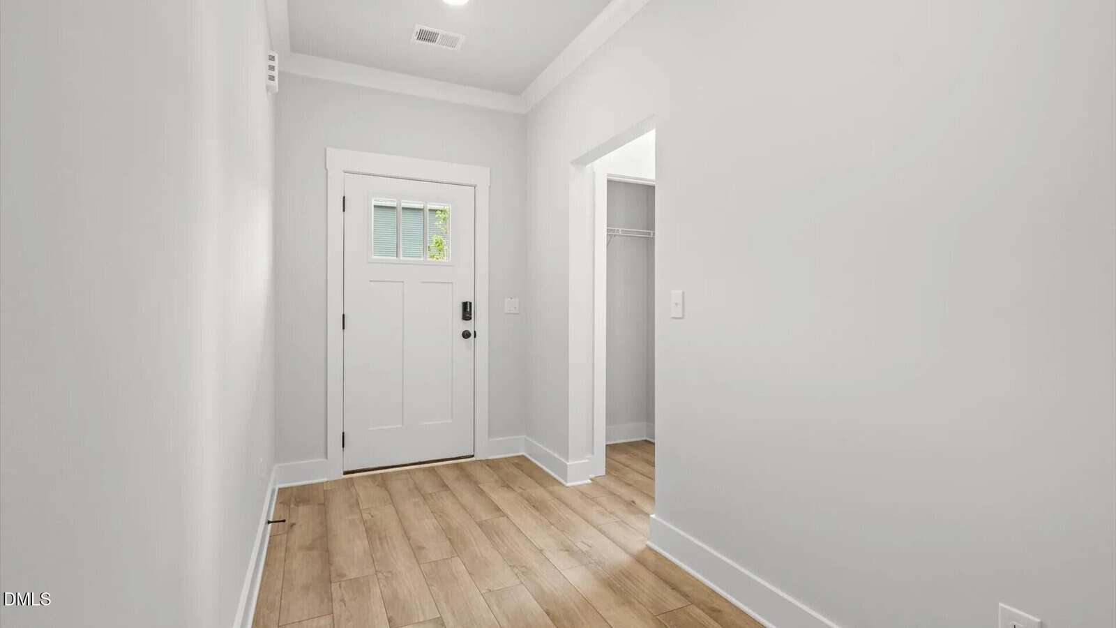 A bright entryway with light wood flooring, white walls, a white front door with a window, and an open doorway leading to a small closet.
