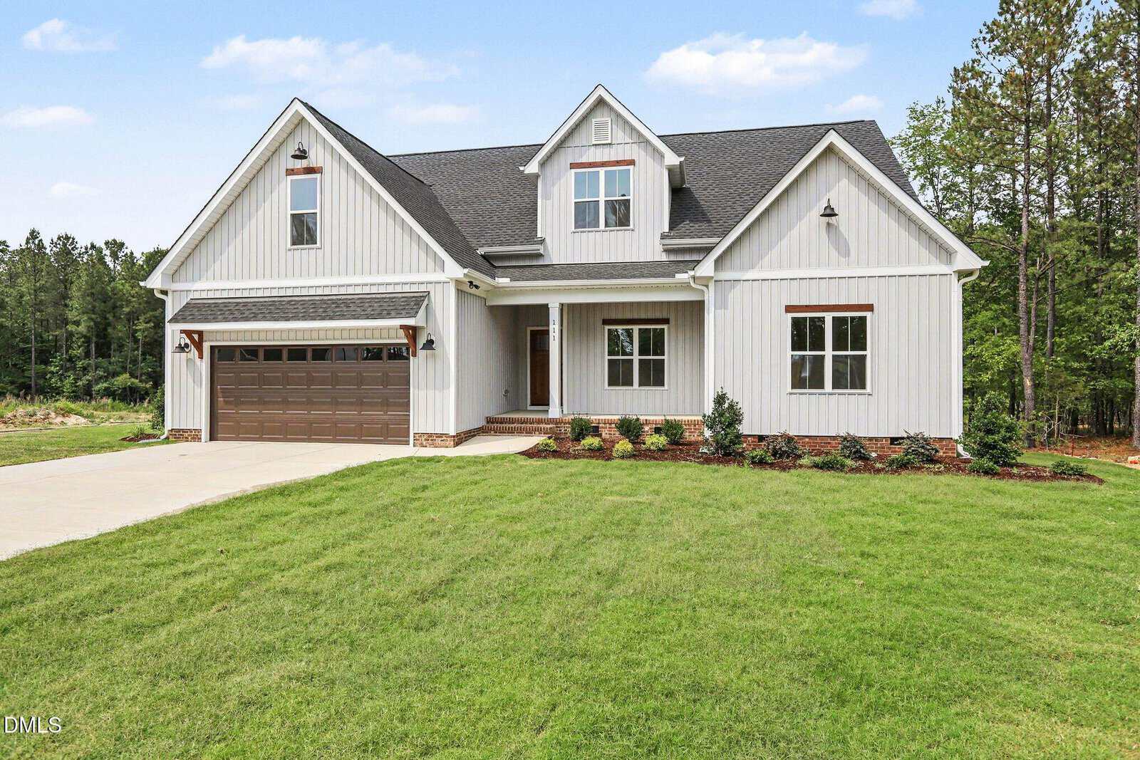 Modern two-story white house with a dark gray roof, attached two-car garage, front porch, and well-maintained lawn, set against a backdrop of trees and blue sky.