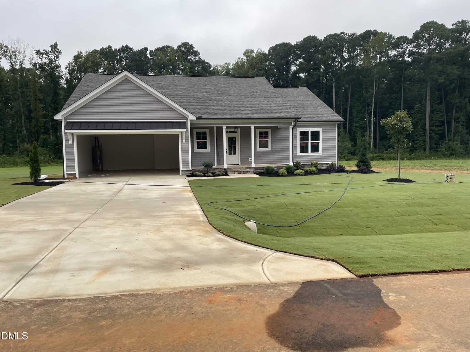 Single-story gray house with two-car garage, front porch, fresh landscaping, and new sod lawn at 12837 Cricket Cove in Zebulon, set against a backdrop of tall trees under an overcast sky.