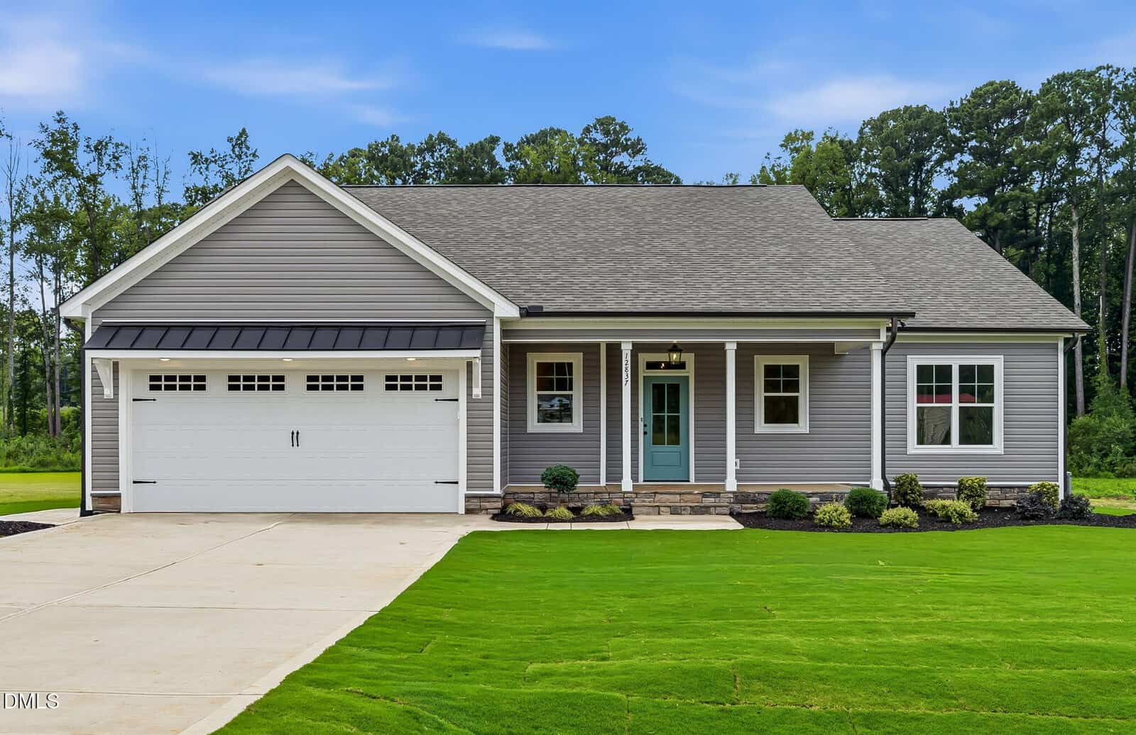 A modern single-story house with gray siding, a two-car garage, a blue front door, white trim, and a large green lawn, set against a background of trees and a blue sky.