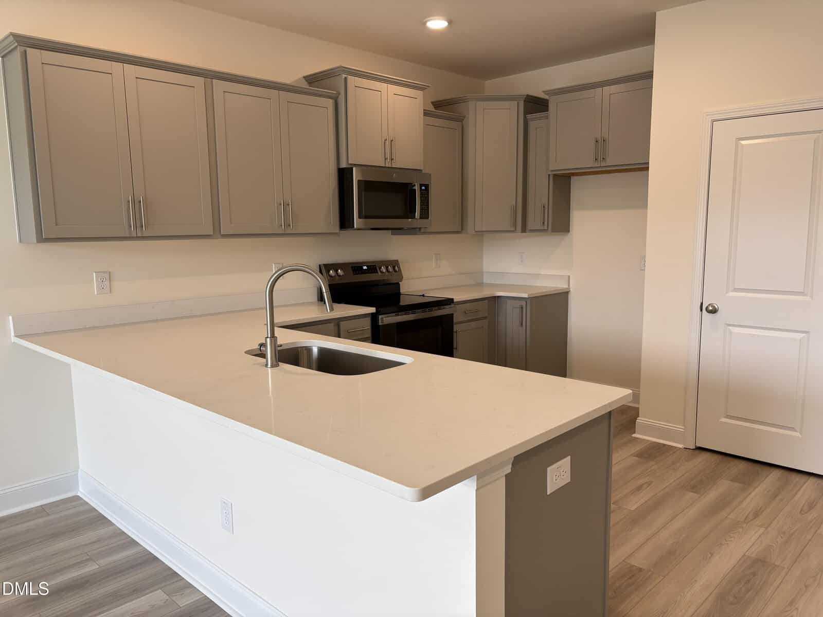 Modern kitchen with light gray cabinets, stainless steel appliances, white quartz countertops, a built-in sink, and light wood flooring. The space is well-lit and features a clean, minimalist design.