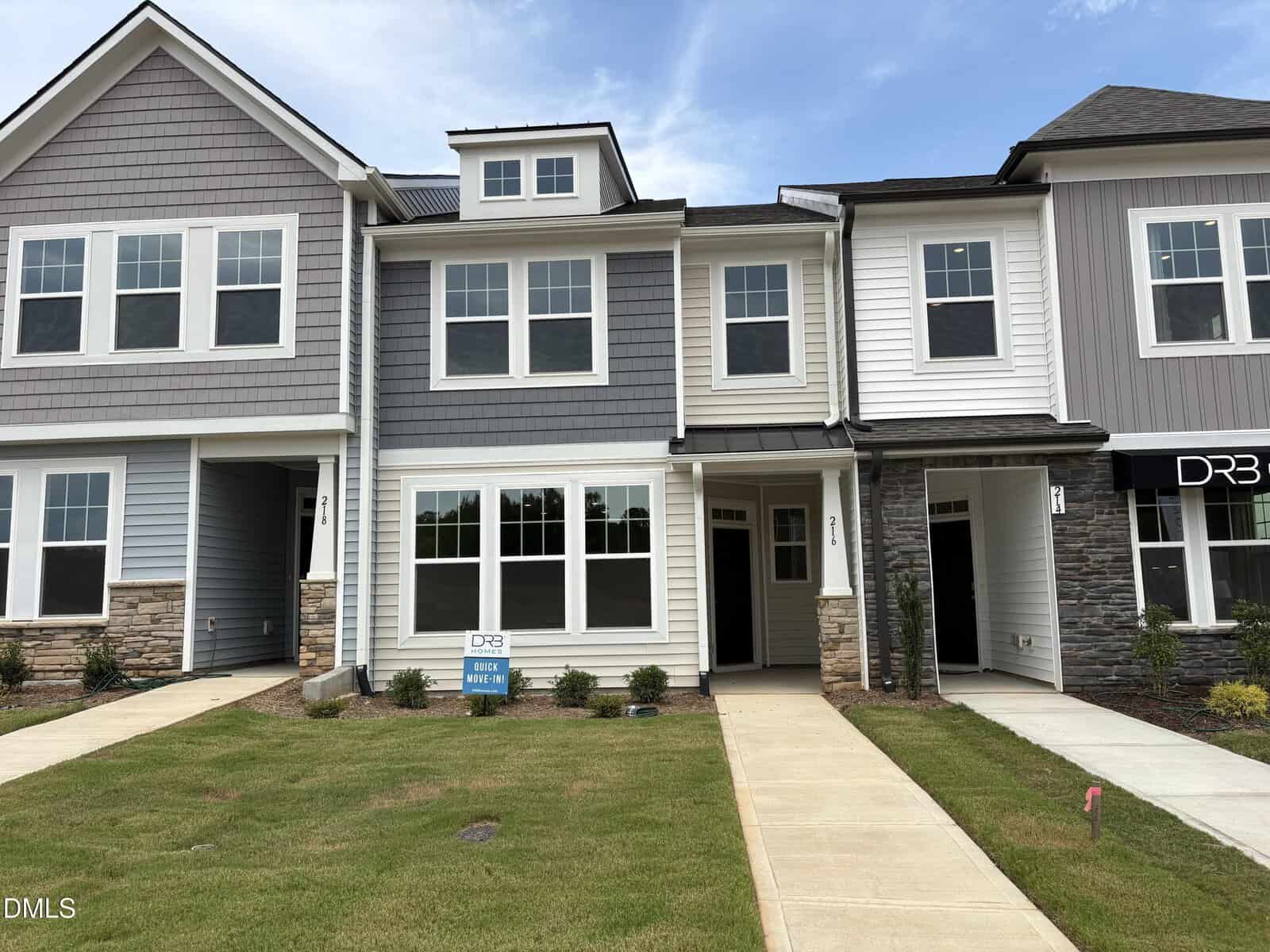 A row of modern two-story townhouses with gray siding and stone accents, large front windows, and manicured lawns lines 216 Straight Lane in Franklinton. A “DRB” real estate sign is visible in front of the center unit.