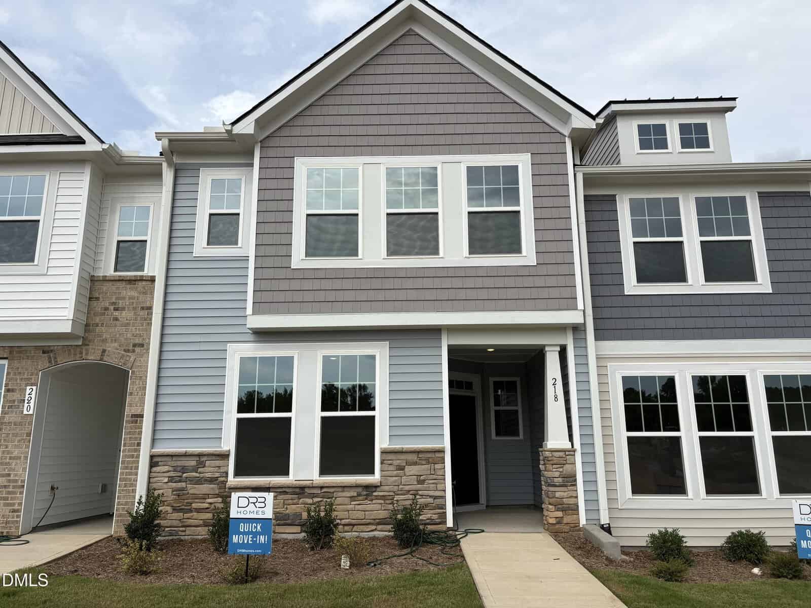 Two-story townhouse at 218 Straight Lane, Franklinton, featuring gray siding, stone accents, multiple windows, a covered front porch, and a small lawn with bushes. Real estate signs are visible near the sidewalk.