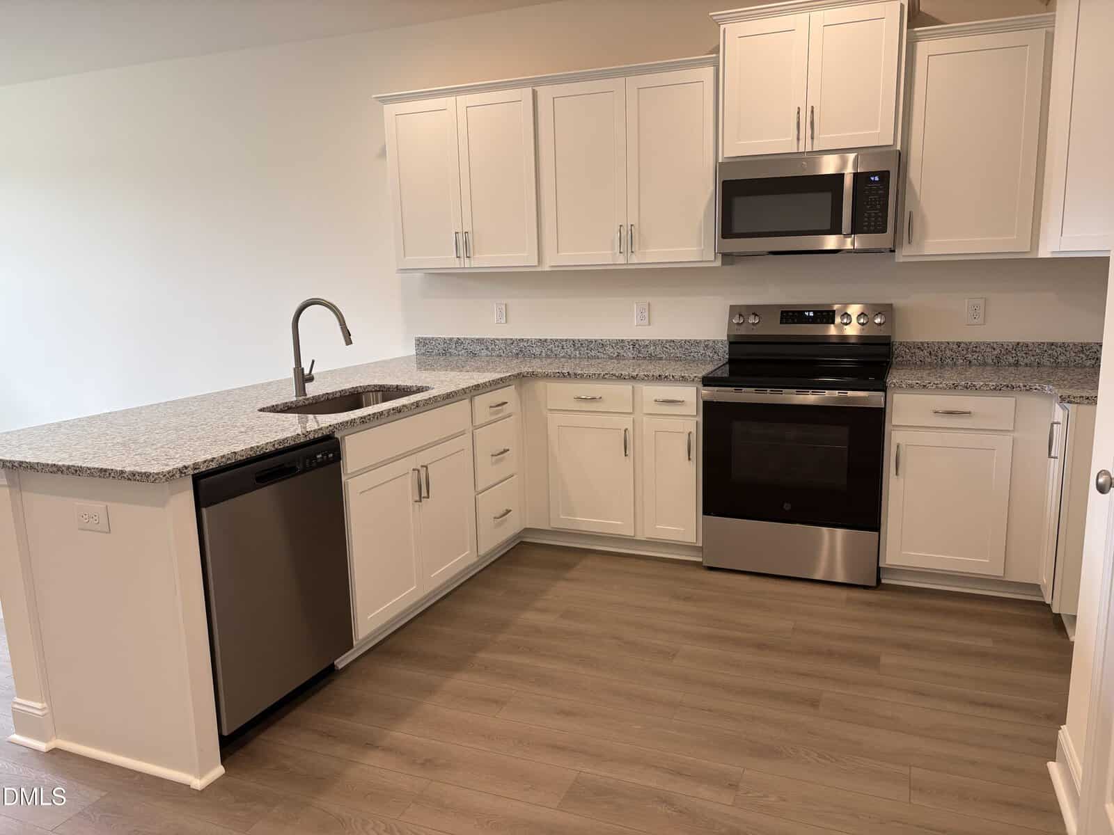Modern kitchen with white cabinets, granite countertops, stainless steel appliances including a stove, microwave, and dishwasher, and light wood flooring. The kitchen has an L-shaped layout with a sink on the counter.
