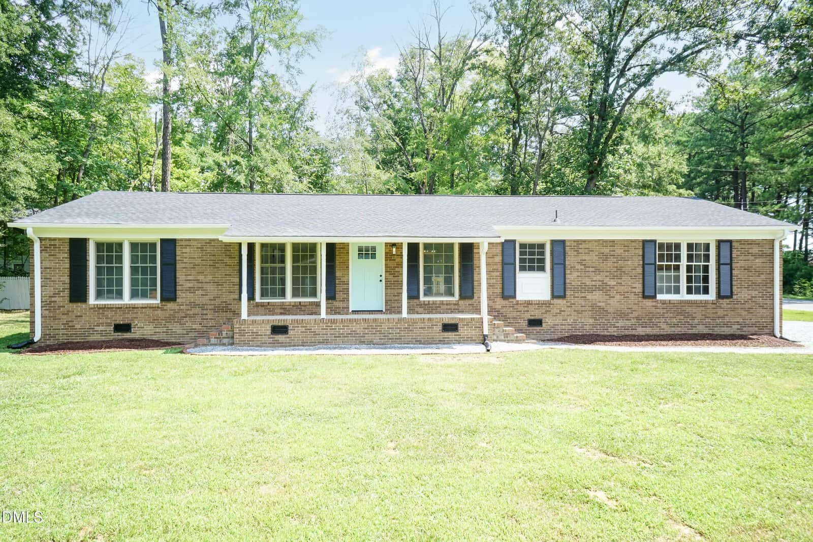 Single-story brick house with black shutters, white trim, and a centered white front door, set on a grassy lawn with trees in the background on a sunny day in Butner at 200 12th Street.