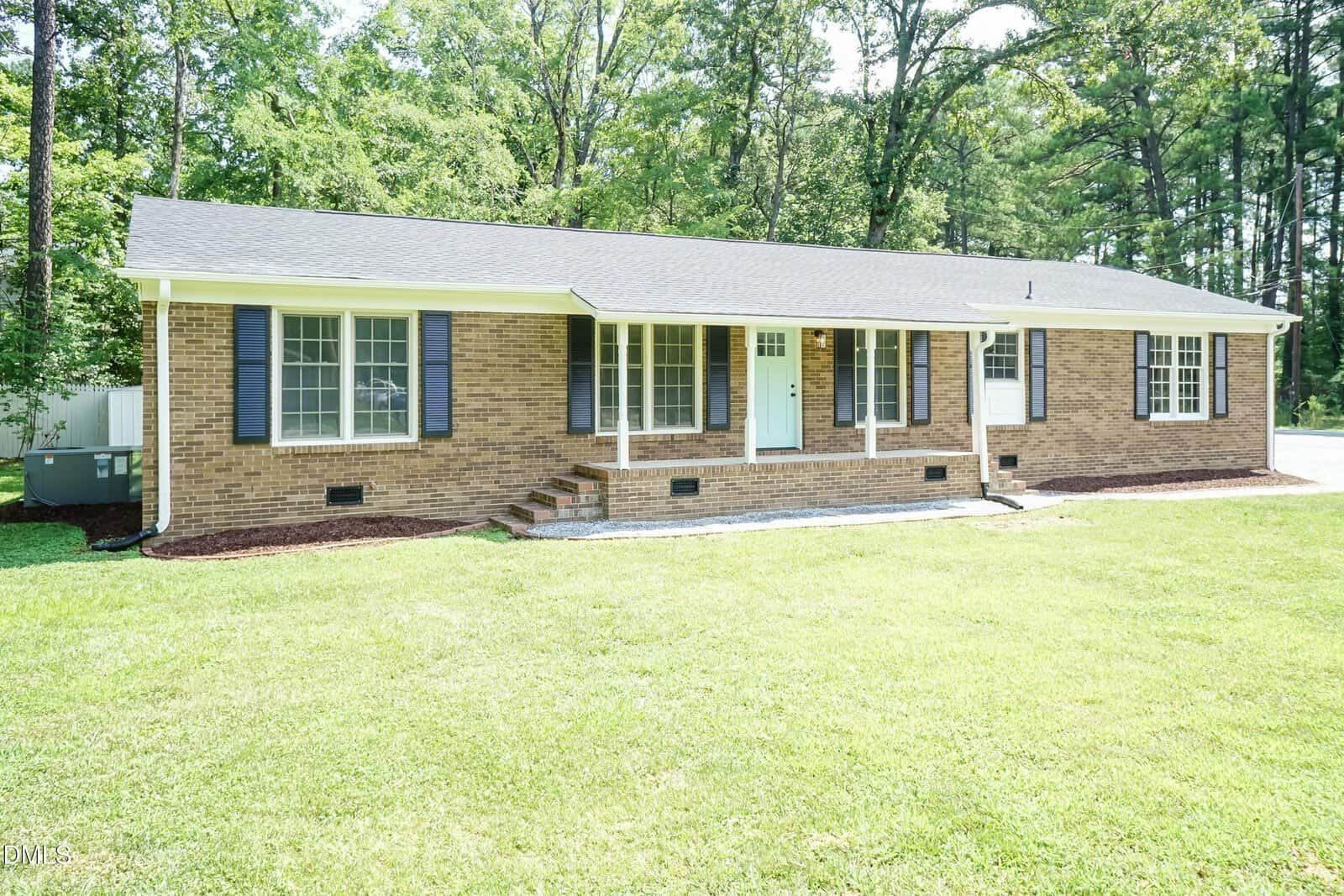 Single-story brick house with black shutters, large front windows, a light blue door, small front steps, and a well-kept green lawn, surrounded by trees.