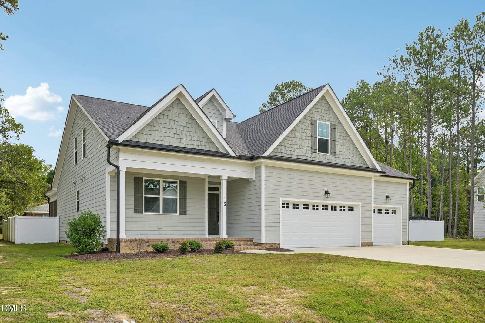 A modern two-story house with light gray siding, white trim, an attached three-car garage, and a covered front porch, set on a grassy lot with trees in the background at 15 Arbor Drive in Youngsville.