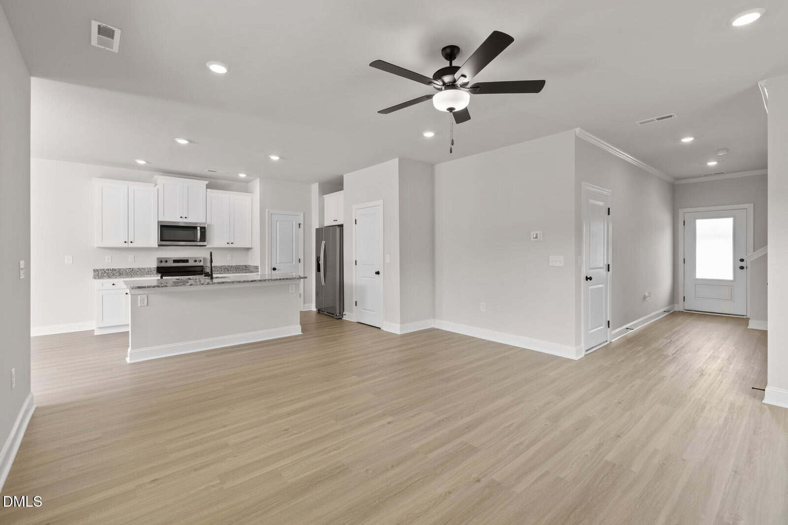 Modern open-concept kitchen and living area with light wood floors, white cabinets, stainless steel appliances, ceiling fan, recessed lighting, and a door leading to the outside.