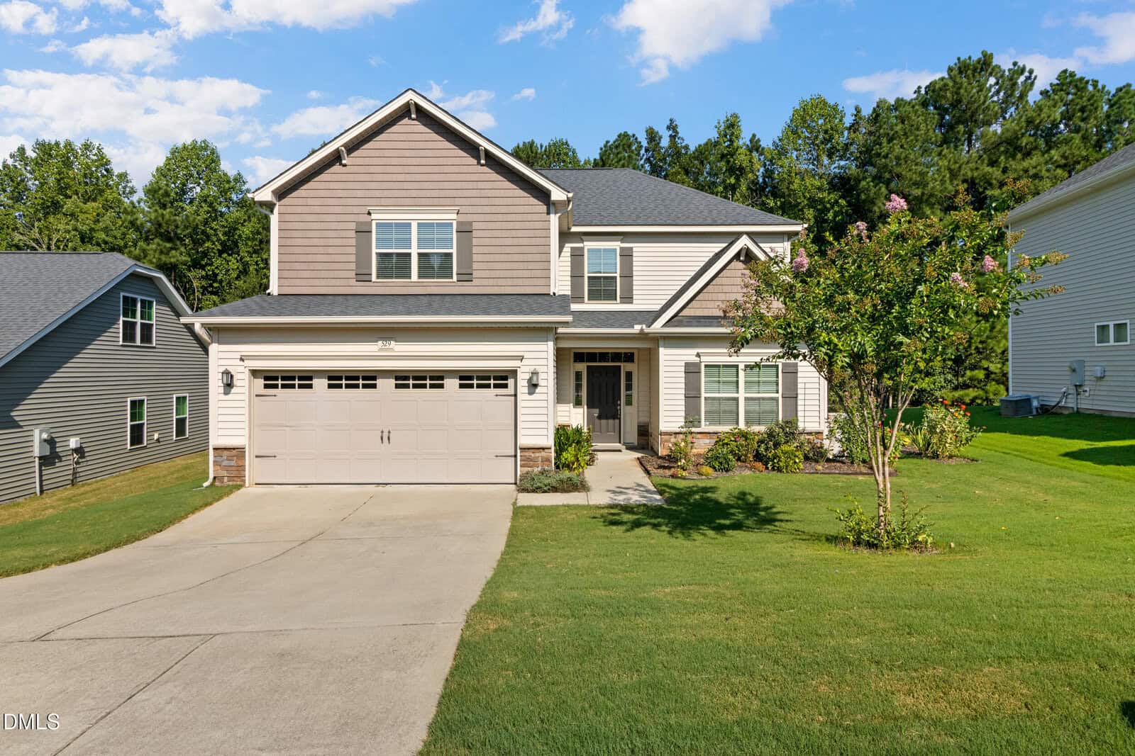 Two-story suburban house with gray siding and a double garage, surrounded by a green lawn and trees at 529 Holden Forest Drive in Youngsville. There’s a concrete driveway and some landscaping near the front entrance under a partly cloudy sky.