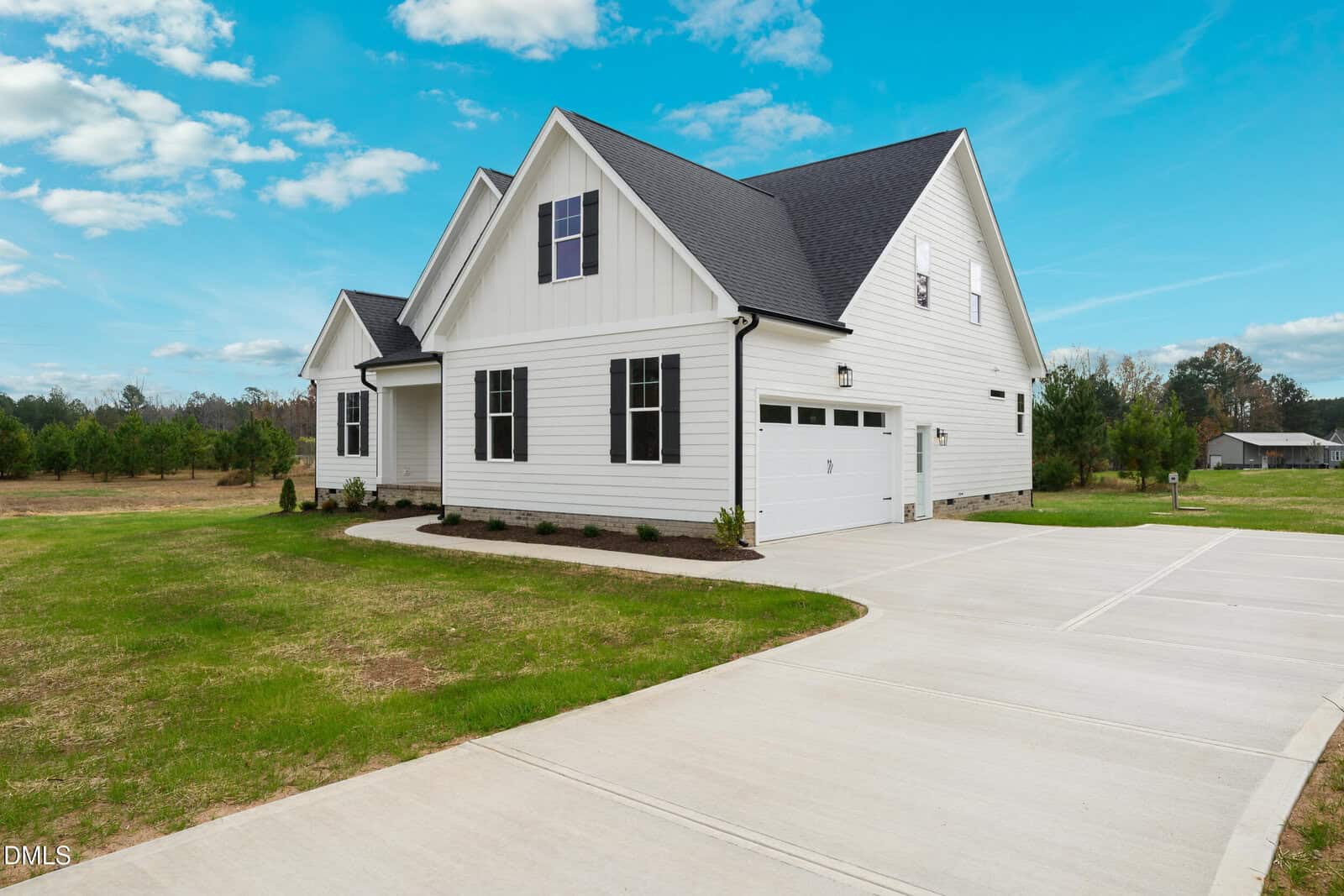 White modern house with black roof, attached two-car garage, large driveway, and manicured lawn at 30 Bella Lane in Zebulon. Trees and a field are in the background under a bright blue sky with scattered clouds.