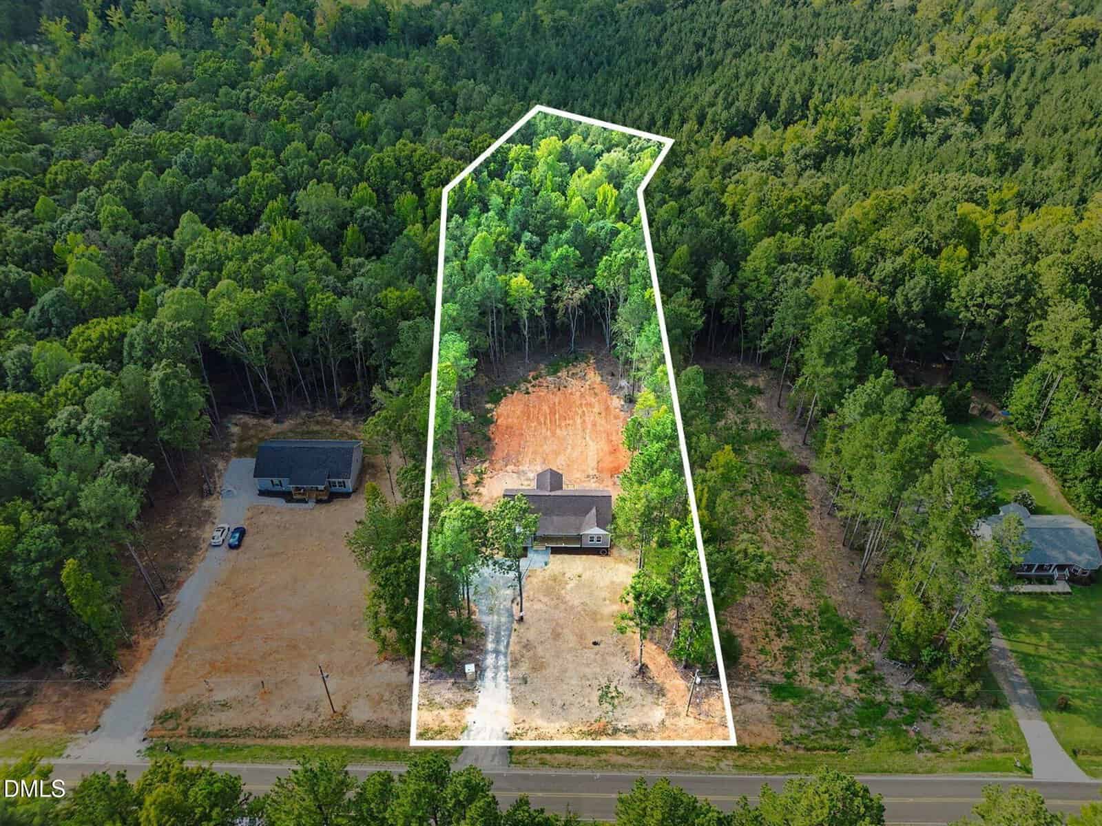 Aerial view of a wooded property with a house and driveway, outlined in white, surrounded by trees and neighboring homes. Forested area is visible behind the house.