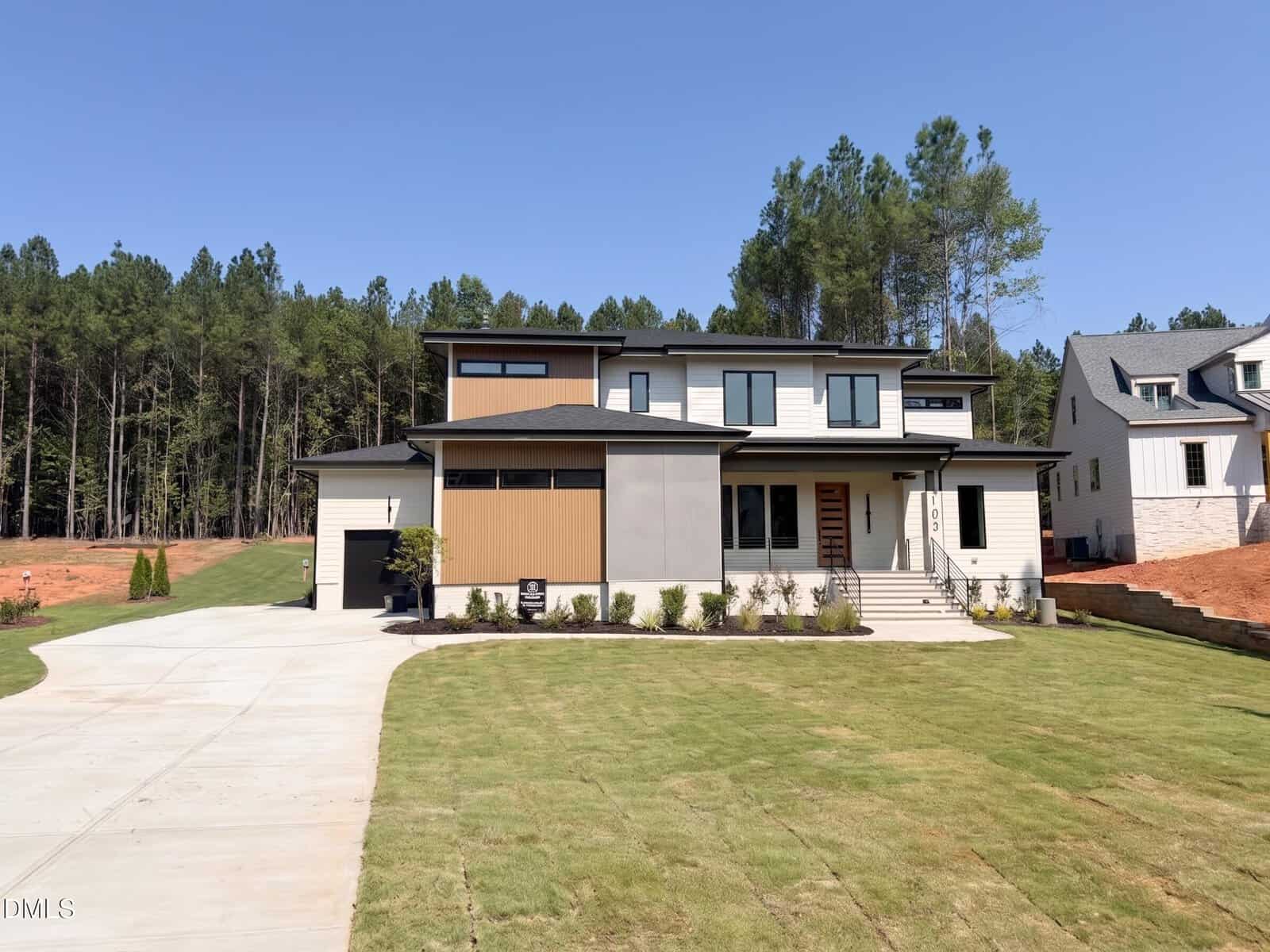 Two-story modern house with large windows, a mix of beige and gray siding, and a single-car garage, situated on a freshly sodded lawn with trees and clear sky in the background at 105 Spanish Oak Drive in Youngsville.