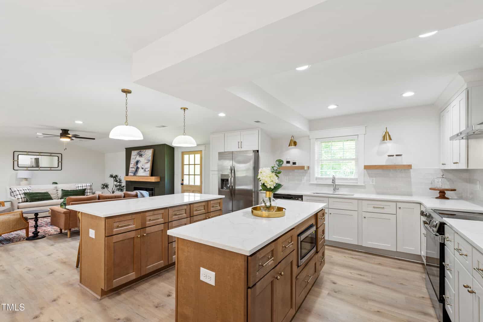 Modern open kitchen with marble countertops, wood and white cabinets, stainless steel appliances, island seating, pendant lighting, and a view into a living area with a sofa, coffee table, and fireplace—perfectly situated in the charming town of Louisburg at 5905 NC 561 Highway.