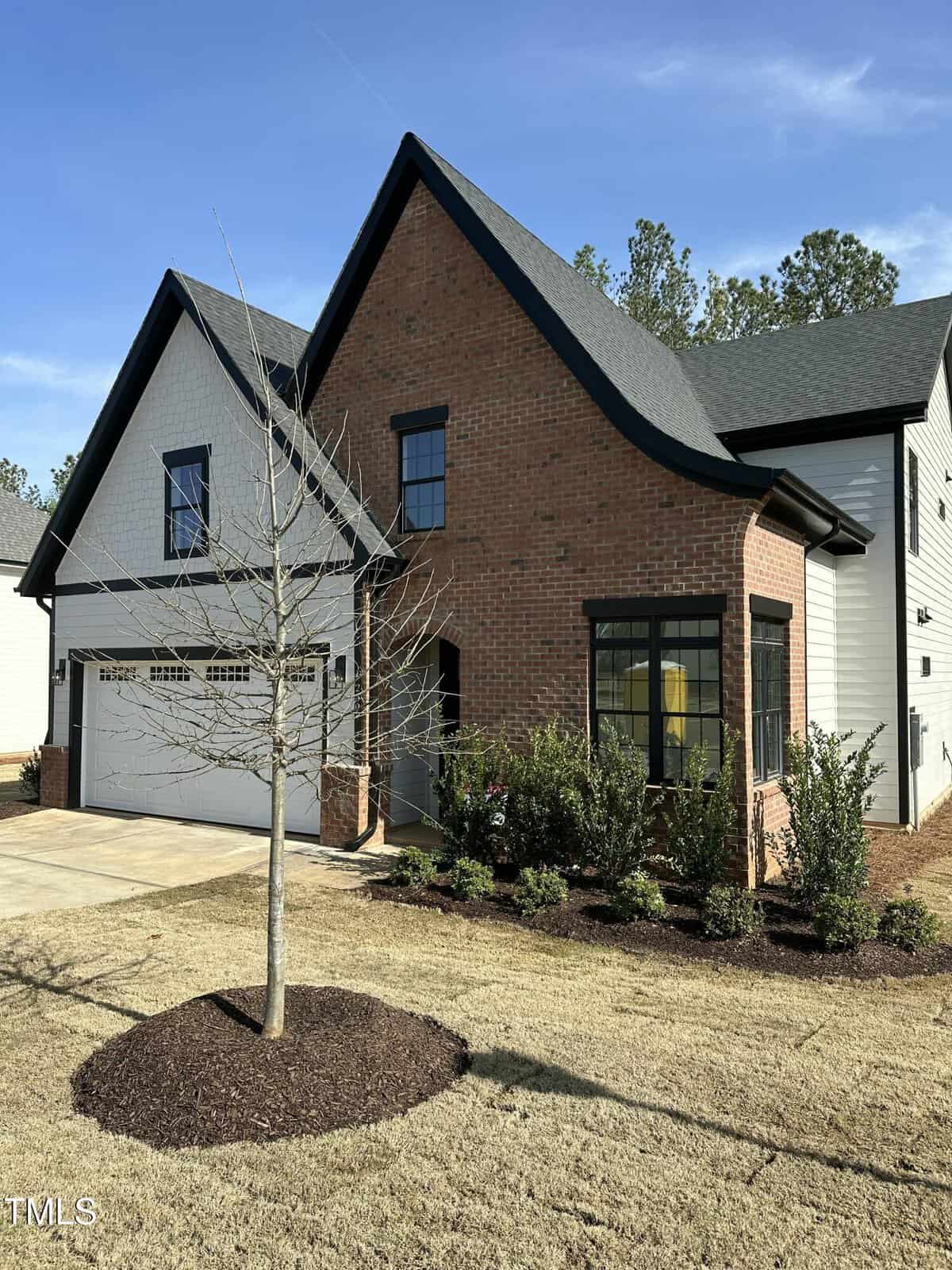 A modern two-story house at 230 Sutherland Drive, Franklinton, featuring a striking brick and white siding exterior with black trim, a spacious two-car garage, and a neatly landscaped front yard adorned with a young tree and manicured bushes.
