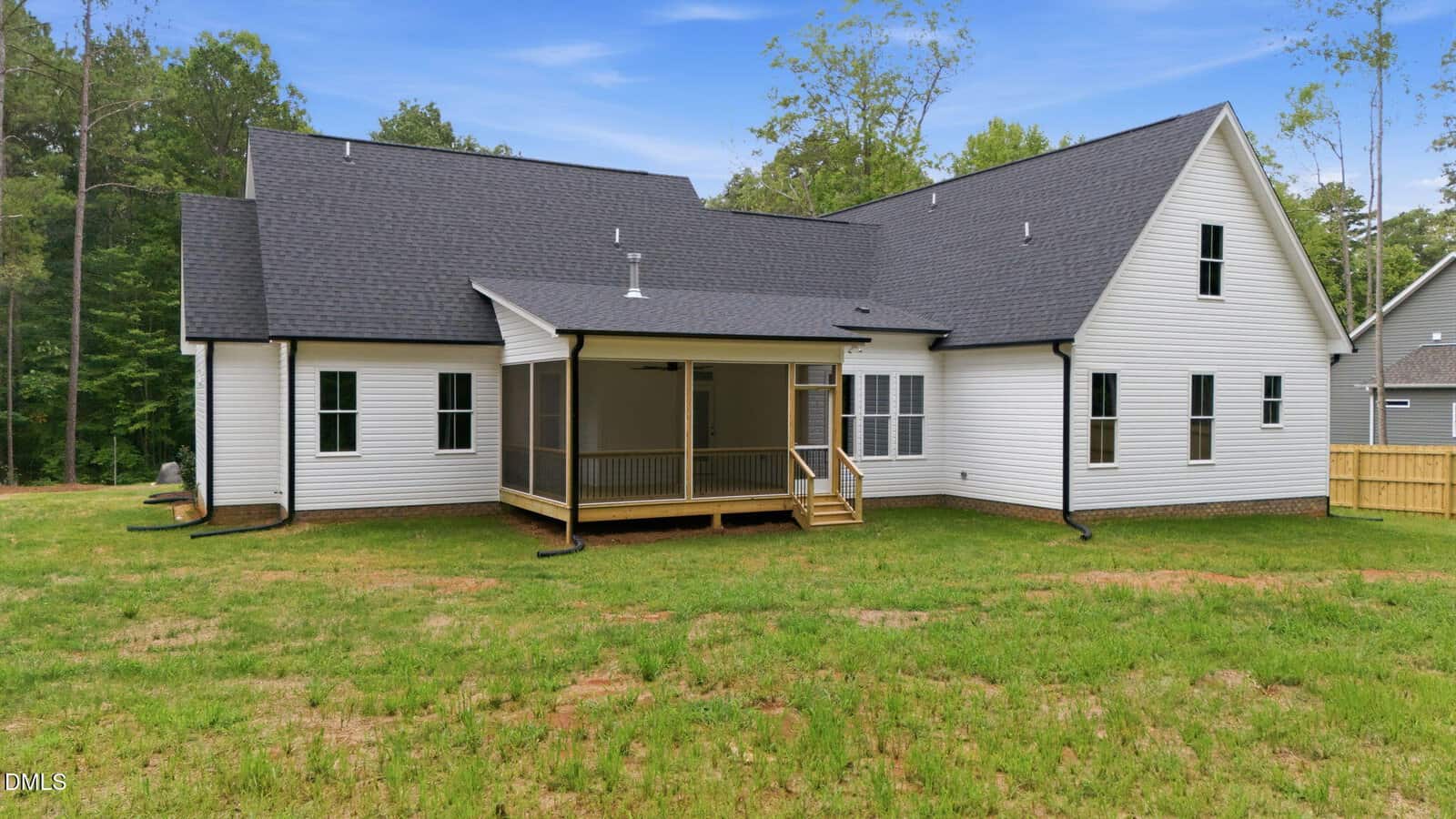 Back view of a modern white house with black roof, screened-in porch, wooden steps, and spacious grassy yard bordered by trees and a wooden fence.