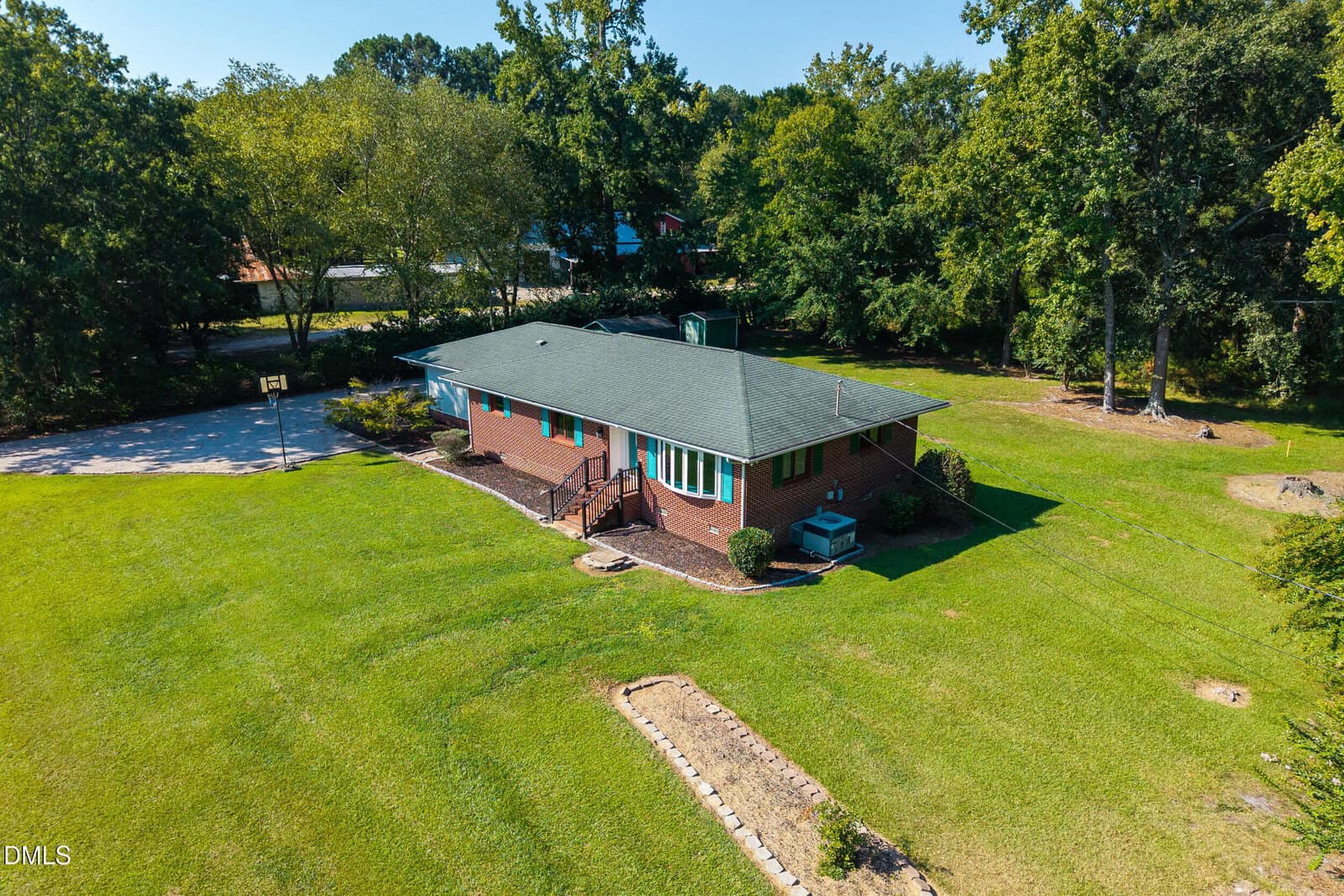 Aerial view of a single-story brick house with a green roof, surrounded by a large, neatly mowed lawn and trees in the background at 402 Stallings Road, Zebulon. A paved driveway and basketball hoop are visible on the left.
