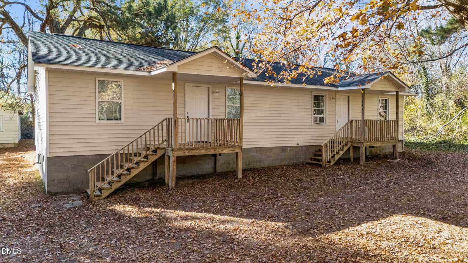 Charming single-story beige house at 691-693 Boddie Street in Henderson, featuring two front doors, each with a small porch and steps, nestled among autumn trees with fallen leaves carpeting the ground.