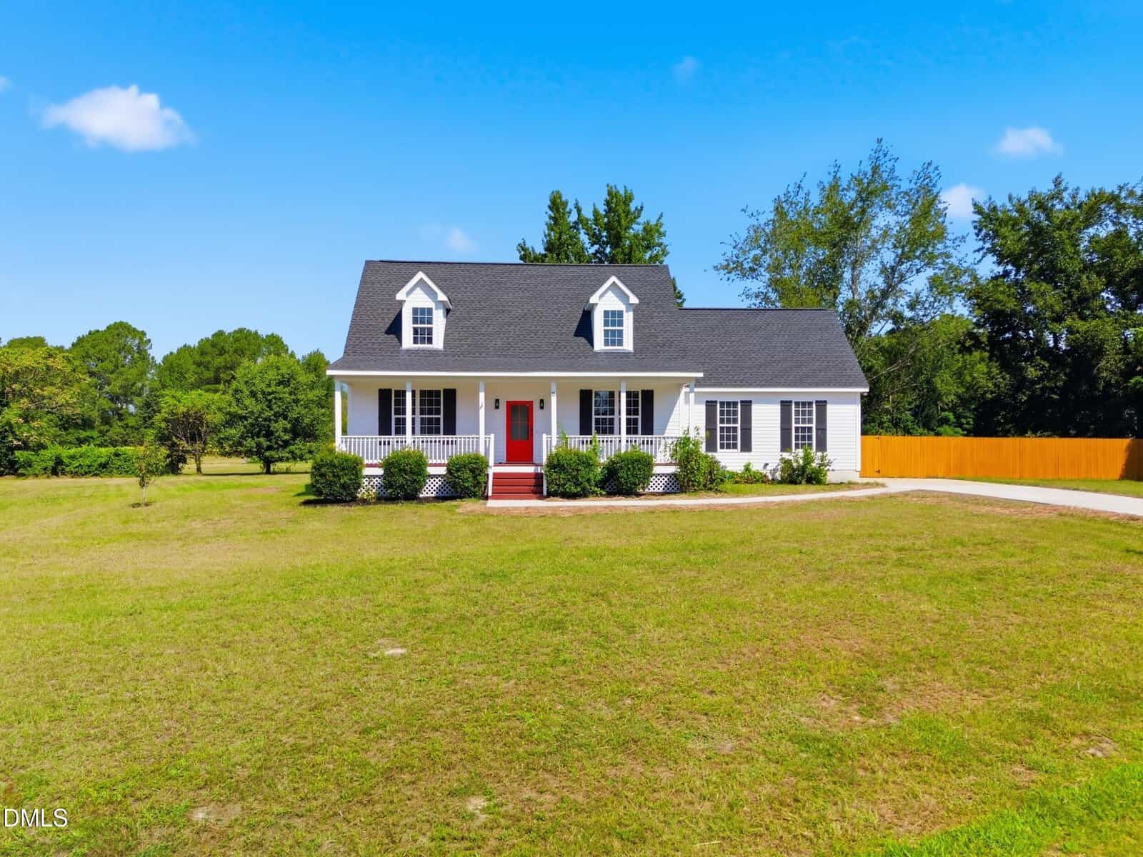 A white house with a black roof and red front door sits on a large, grassy lawn at 15 Davis Cir Drive in Zebulon, with trees in the background under a clear blue sky.