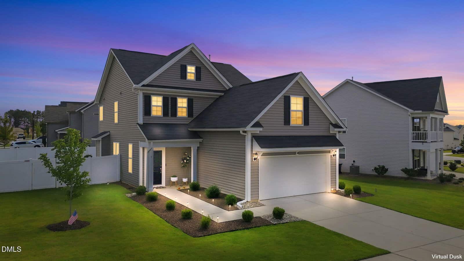 Two-story gray house with white trim at 5 Harpeth Drive, Franklinton, featuring lit exterior lights, an attached two-car garage, manicured lawn and landscaping. Set at dusk with a pink and blue sky, neighboring homes and a fenced backyard are also visible.