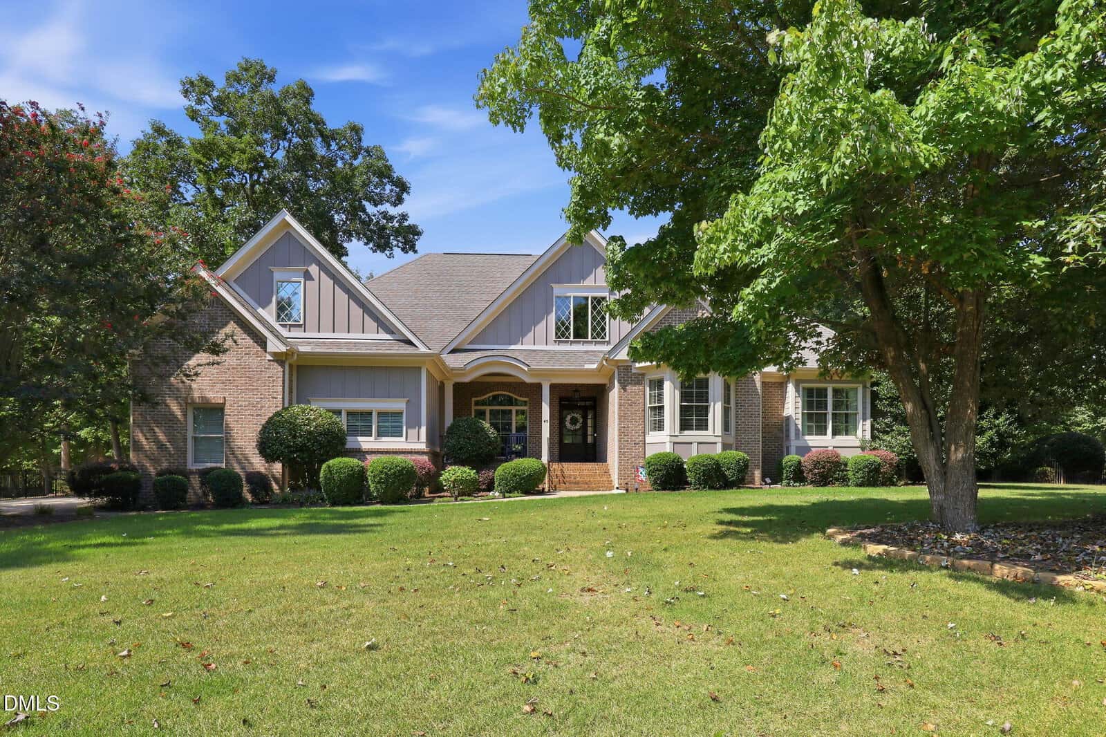 A two-story brick and siding house at 45 Lance Lane in Youngsville features a front porch, dormer windows, manicured bushes, and a large green lawn bordered by trees under a blue sky.