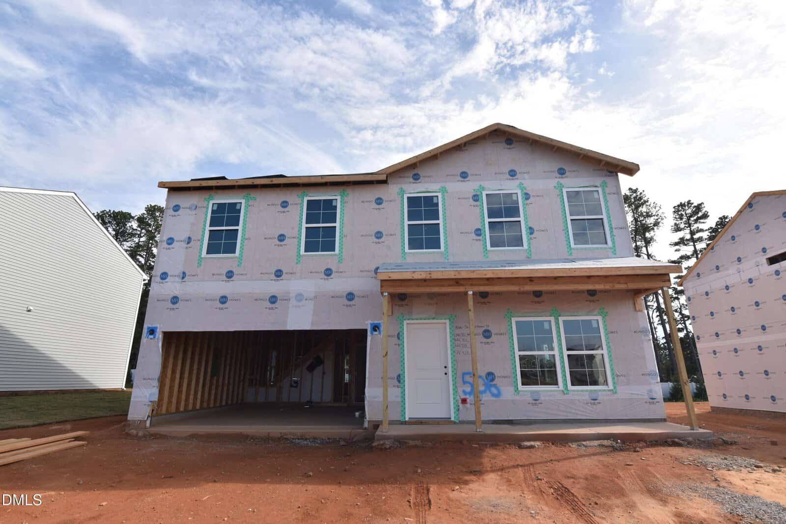A two-story house under construction at 56 Mistflower Drive in Youngsville, with exposed framing, wrap covering the exterior, and an unfinished driveway. The garage is open and some windows lack final trim. Blue sky and nearby houses are visible.