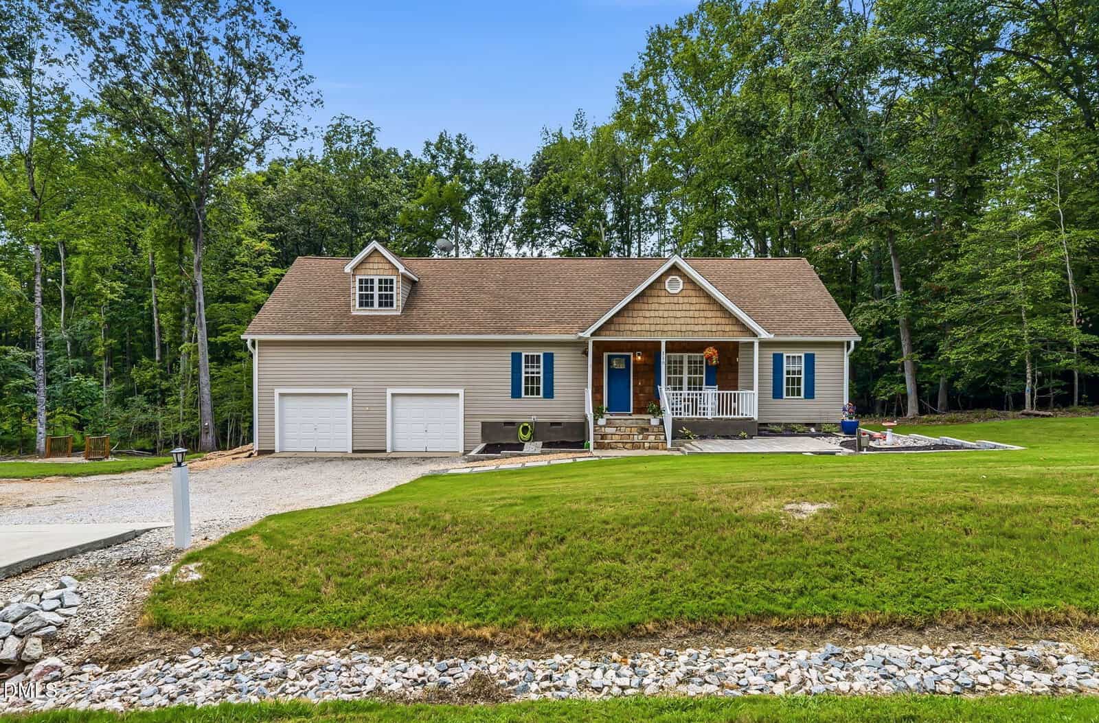 A beige single-story house with an attached two-car garage and front porch, located at 110 Wounded Knee Drive in Louisburg, is surrounded by green grass and trees under a clear blue sky.