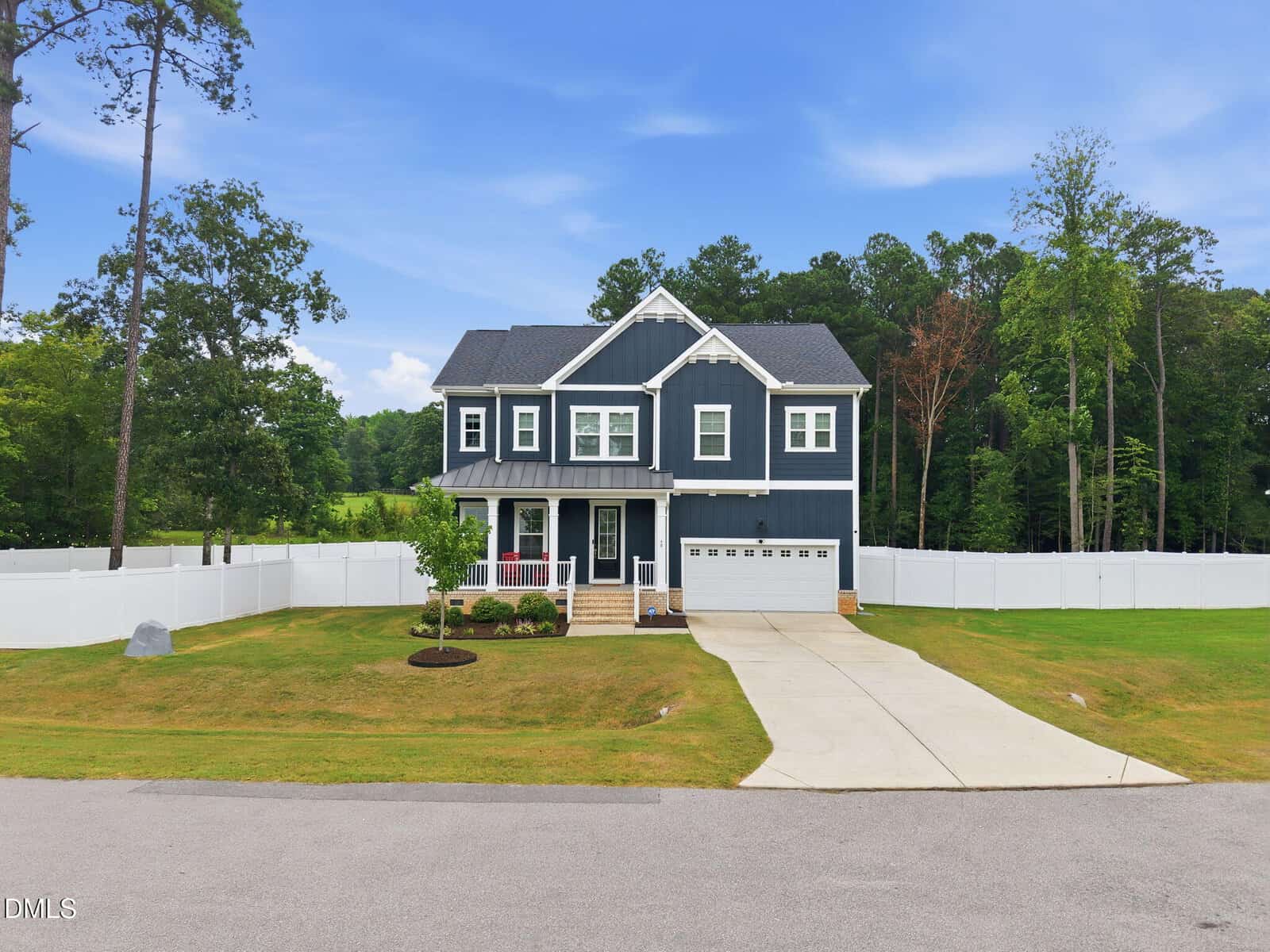 Charming two-story navy blue house with white trim located at 60 Gadwall Court, Zebulon. Features include a welcoming front porch, attached garage, and a wide driveway. Enjoy the neatly cut lawn surrounded by a classic white fence, with trees and a forested area providing a serene backdrop.