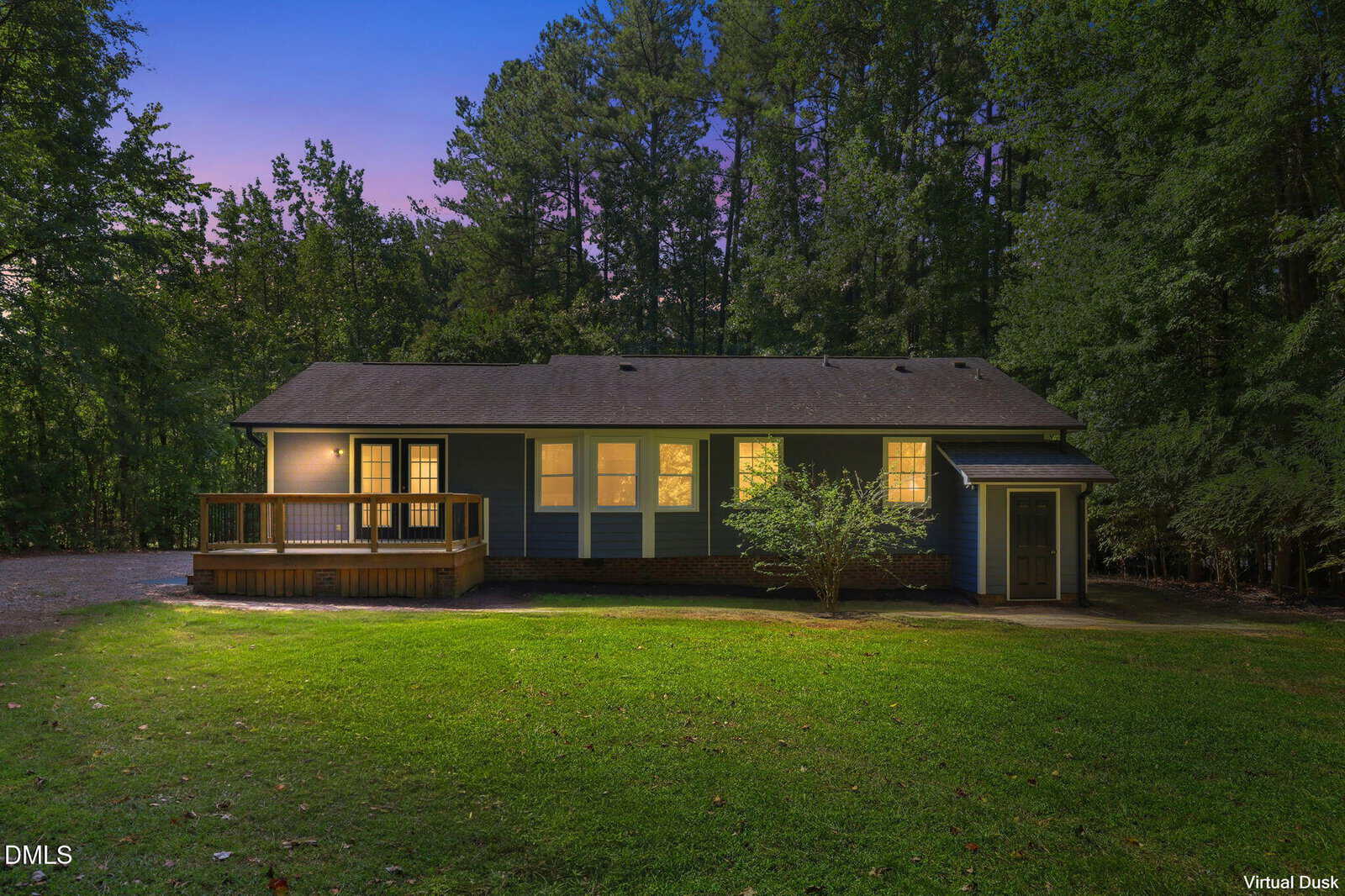 A single-story blue house at 104 Knights Way, Youngsville, with a lit interior, front porch, and surrounding green lawn sits against a backdrop of tall trees at dusk.
