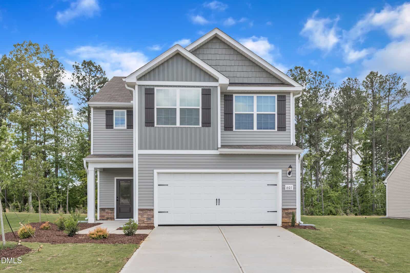 Charming two-story gray house with white trim located at 104 Flue Court, Oxford. Features include a double garage, gable roof, and a beautifully landscaped front yard. Mature trees and a blue sky with clouds provide a picturesque backdrop.