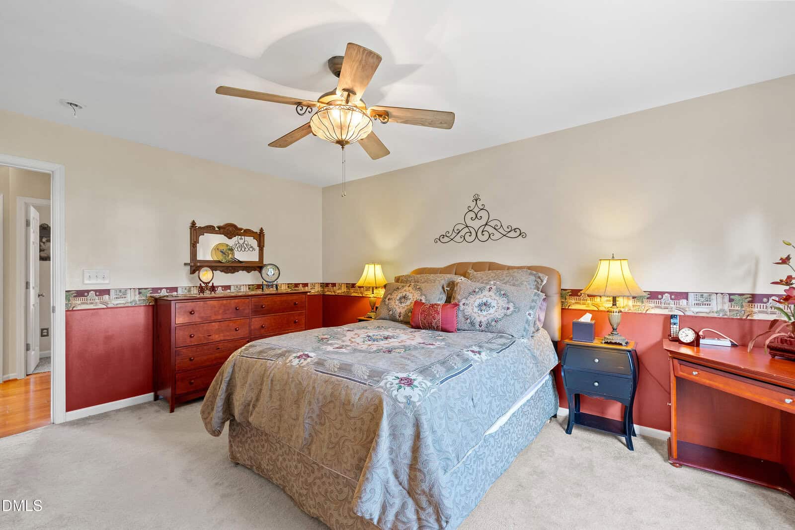 Bedroom at 1968 Bowles Avenue in Creedmoor features a ceiling fan, double bed with patterned bedding, two bedside tables with lamps, a dresser with a mirror, and light carpeted floor. The walls have a decorative border and neutral tones.