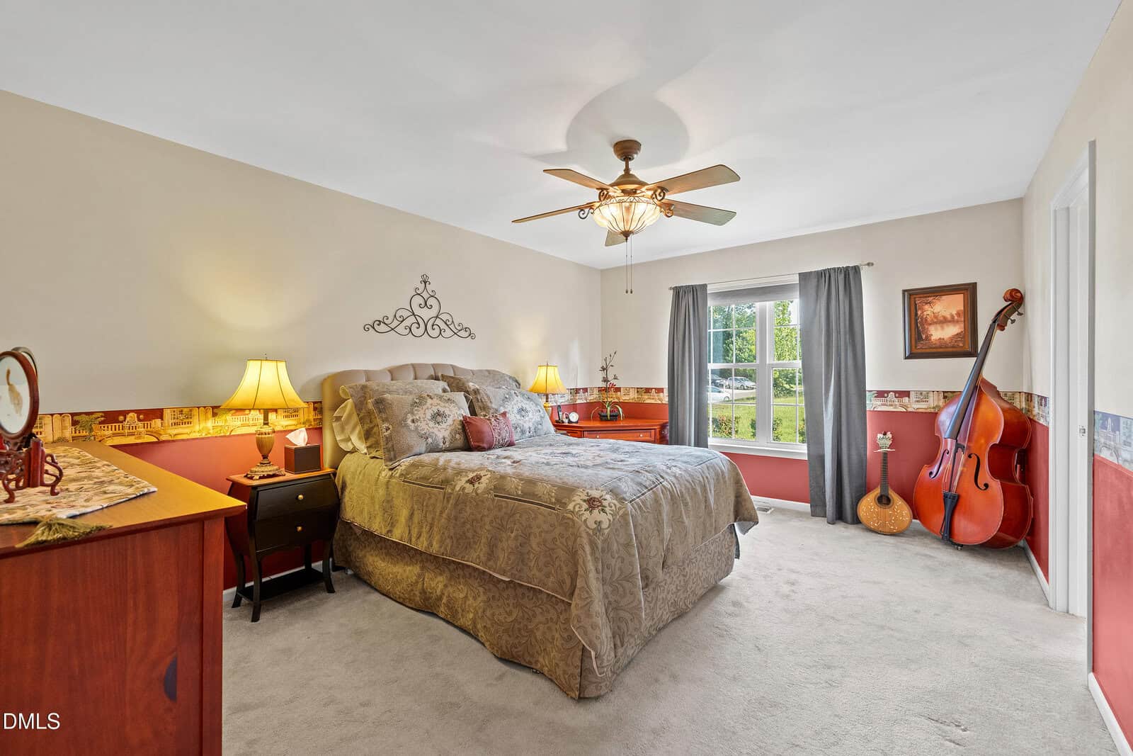A cozy bedroom with a double bed, bedside tables with lamps, a ceiling fan, a large window with gray curtains, and musical instruments including a guitar and double bass in the corner.