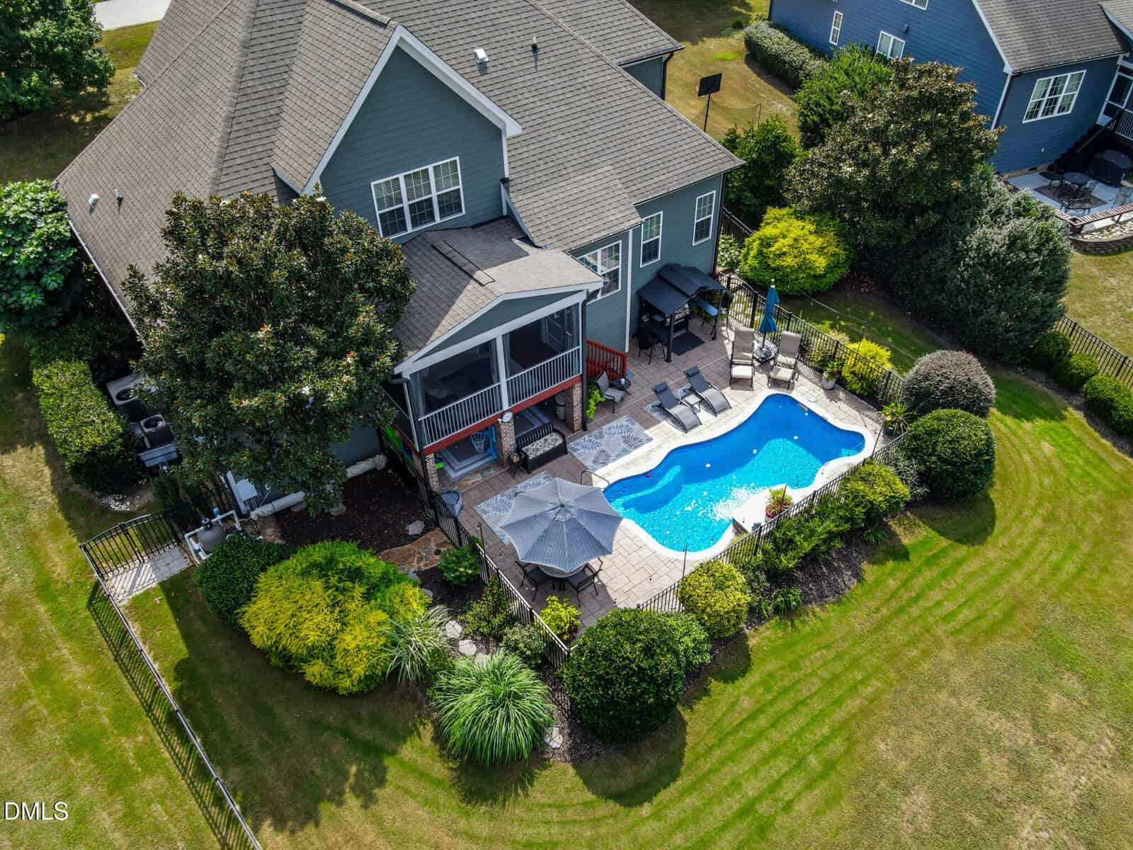 Aerial view of a beautiful two-story house at 60 Cranbrooke Drive, Franklinton, featuring a screened porch, backyard patio, swimming pool, lounge chairs, umbrella, and a landscaped garden surrounded by a fence.