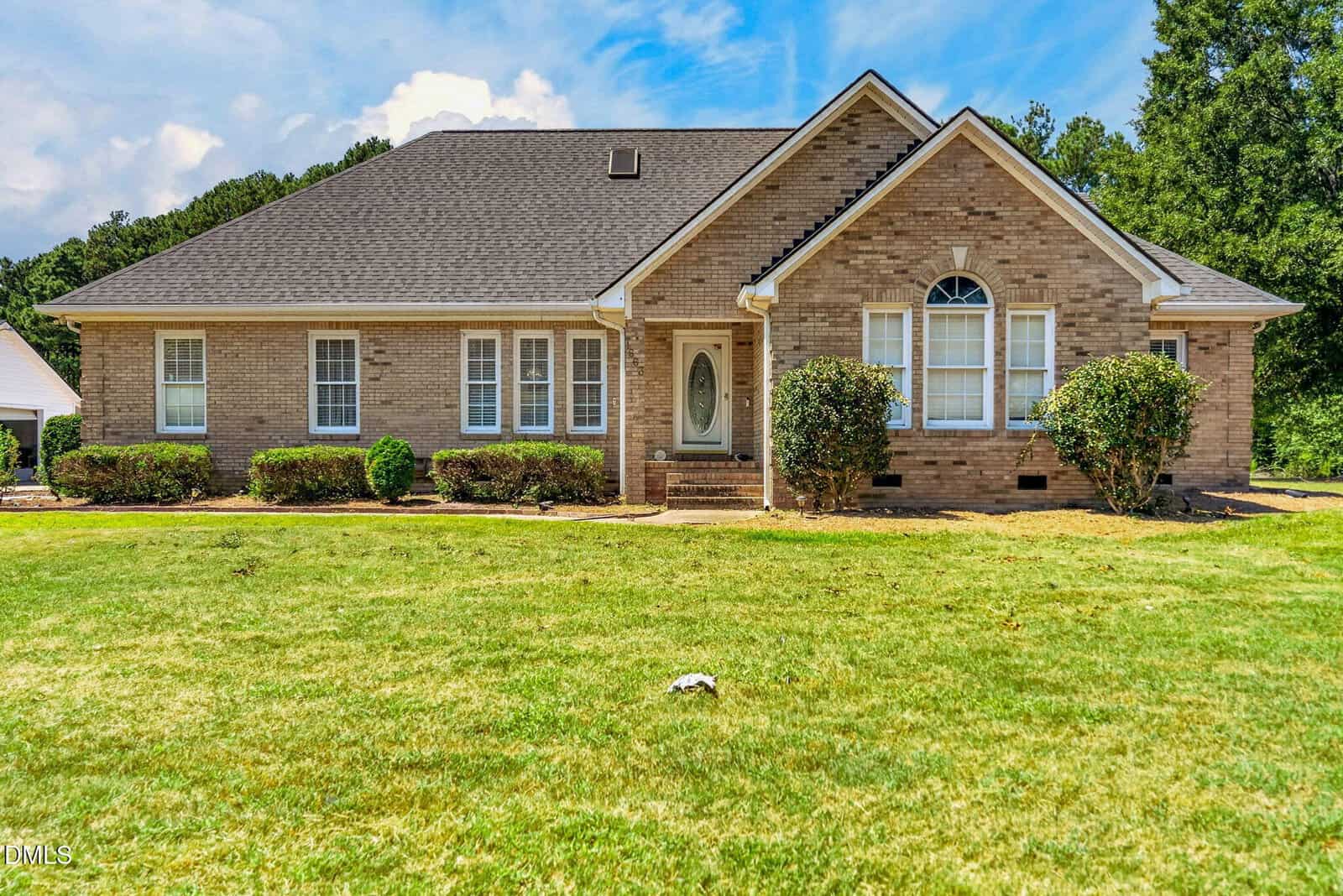 Charming single-story brick house at 1663 Hayes Road, featuring a gable roof, white trim, an arched front window, and shrubs in front—all set on a well-maintained grassy lawn with mature trees and blue skies in the background. Enjoy peaceful living in beautiful Creedmoor.