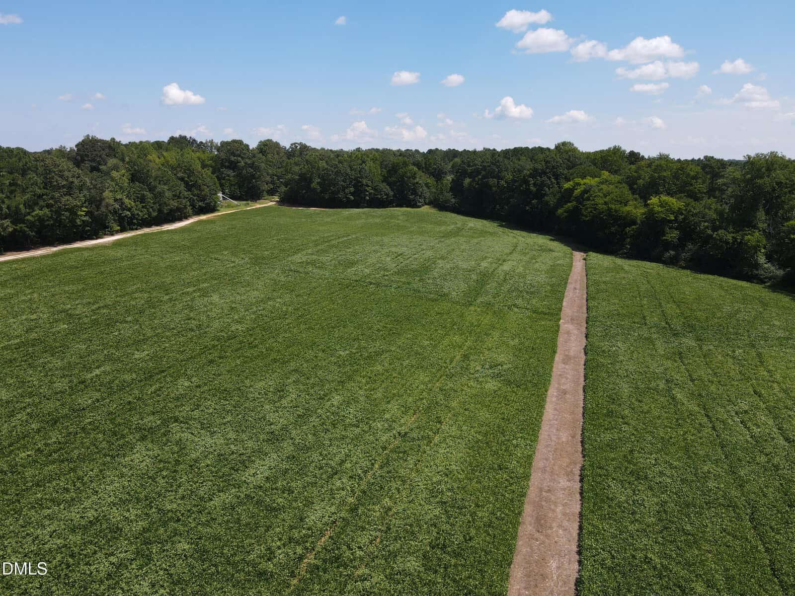 Aerial view of a large green field bordered by trees along 0 Epsom Rocky Ford Road, Henderson, with a dirt path running straight through the middle under a blue sky with scattered clouds.
